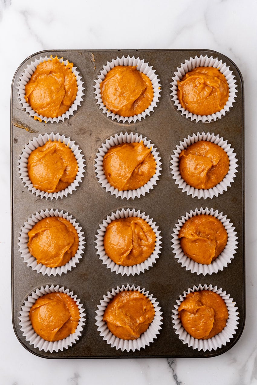 pumpkin muffin batter in white cupcake liners in a metal muffin pan