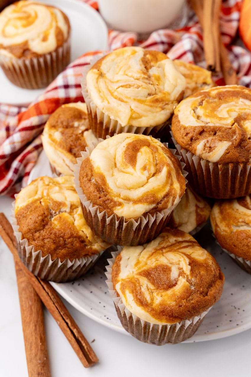 a pile of pumpkin cream cheese swirl muffins stacked on a white plate