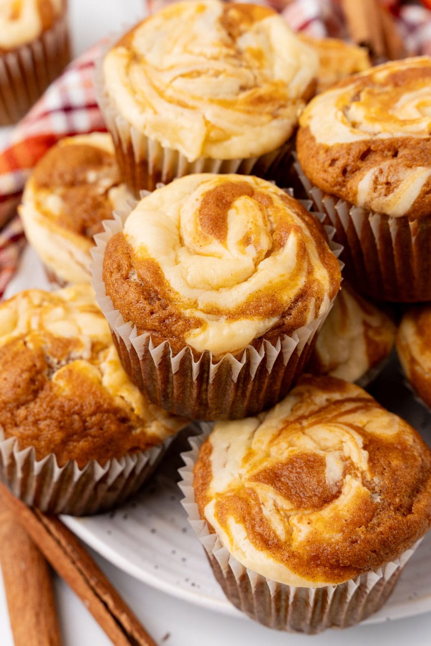 a pile of pumpkin cream cheese swirl muffins stacked on a white plate