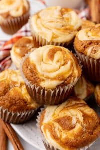 a pile of pumpkin cream cheese swirl muffins stacked on a white plate