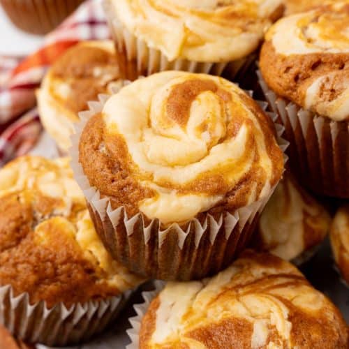 a pile of pumpkin cream cheese swirl muffins stacked on a white plate