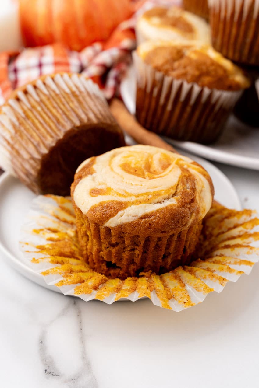 an unwrapped pumpkin cream cheese swirl muffin on a small white dessert plate