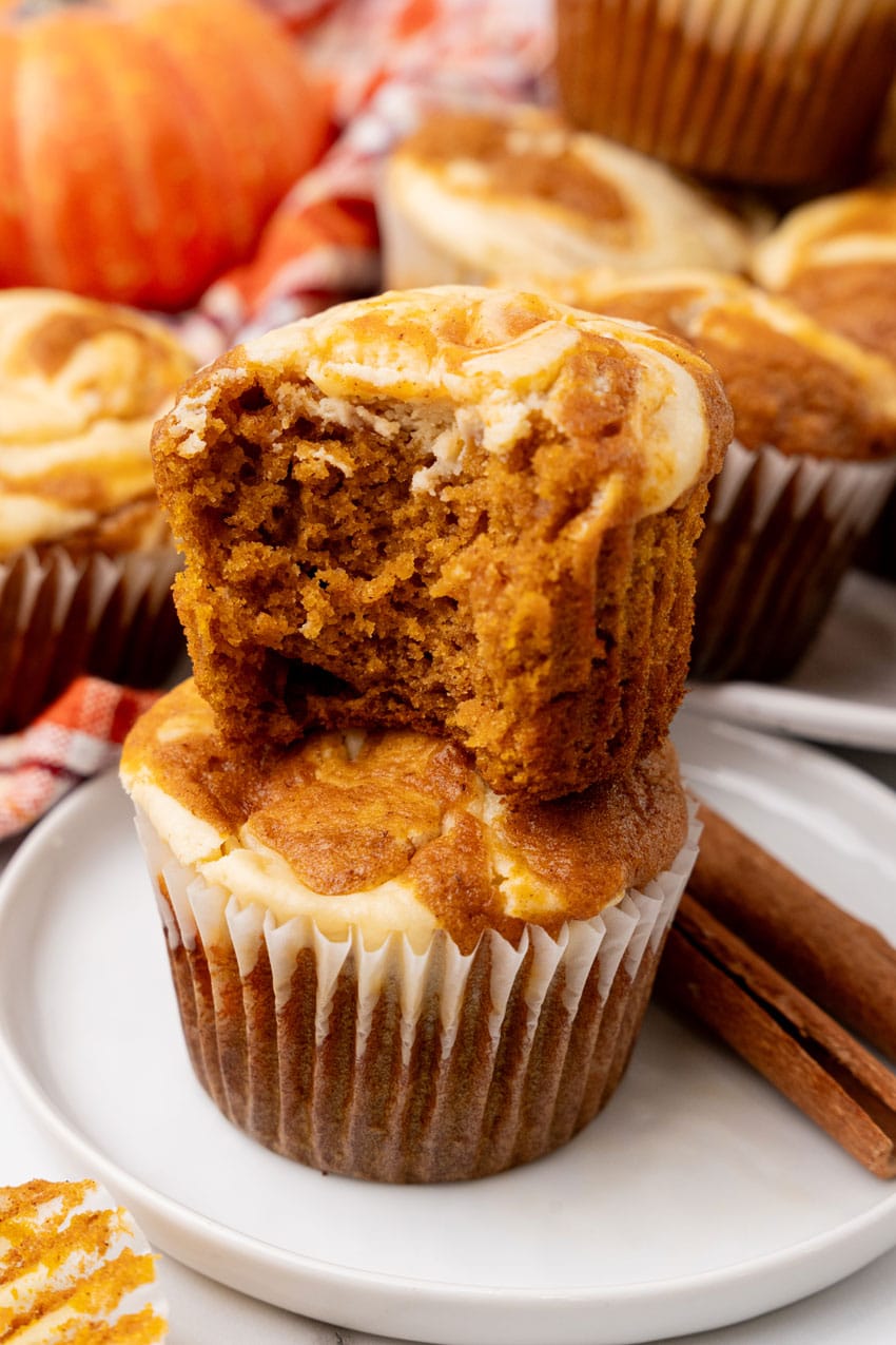 an unwrapped bitten pumpkin muffin sitting on top of another pumpkin muffin on a small white dessert plate