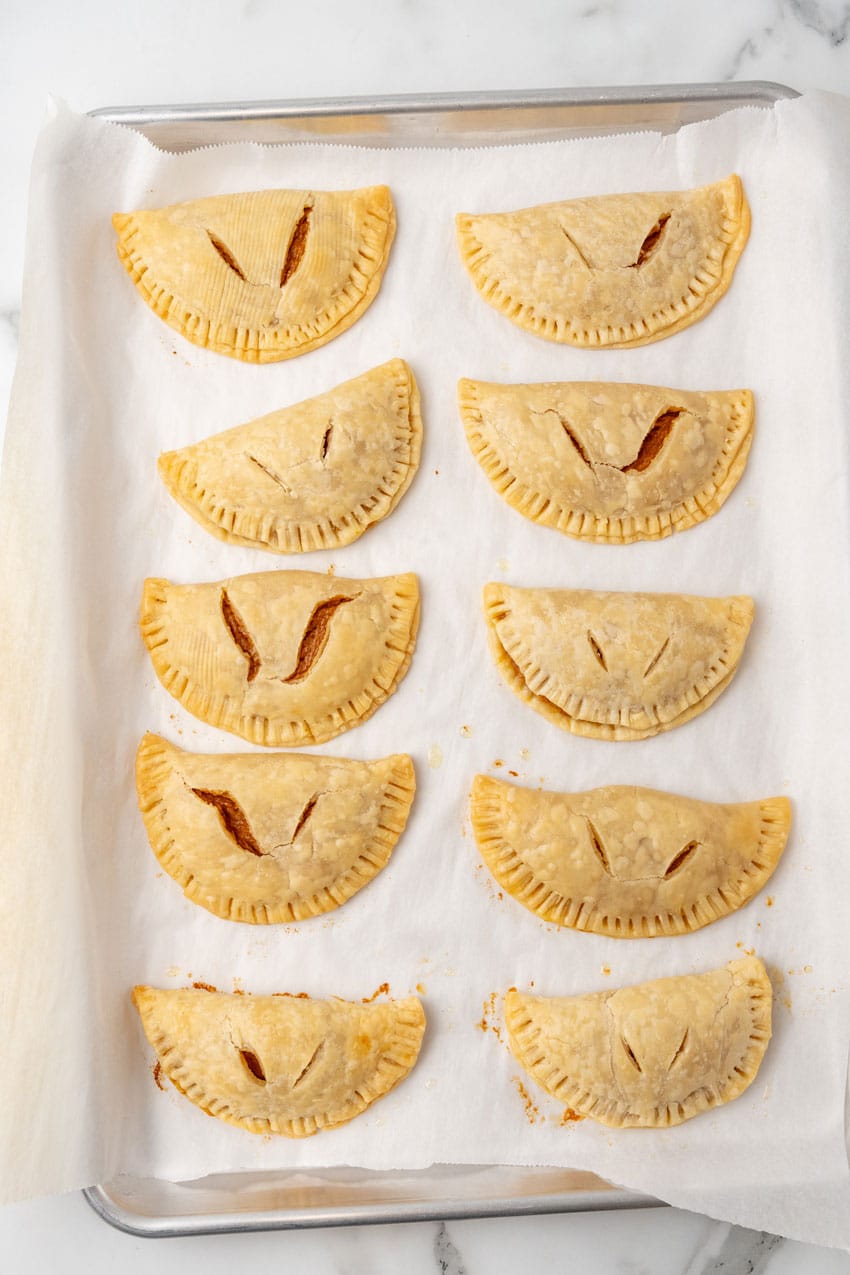 two rows of baked pumpkin hand pies on a parchment paper lined baking sheet