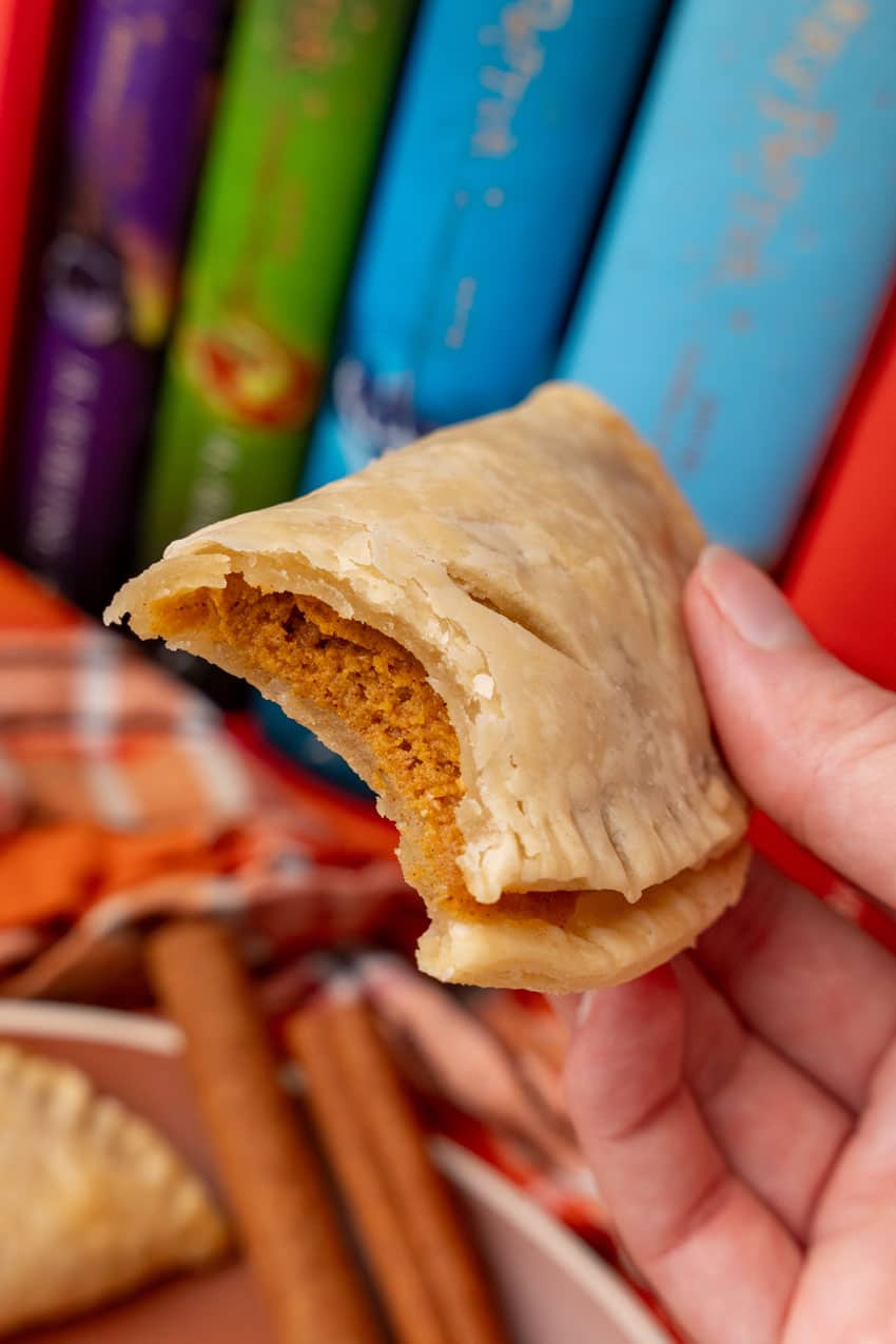 a hand holding up a bitten pumpkin hand pie to reveal the creamy filling