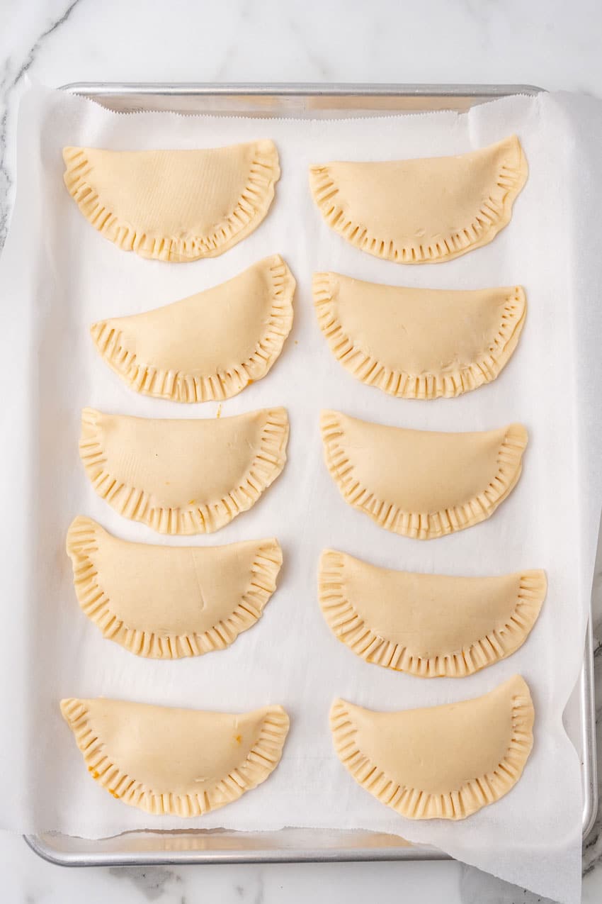 unbaked pumpkin hand pies arranged in two rows on a parchment paper lined baking sheet