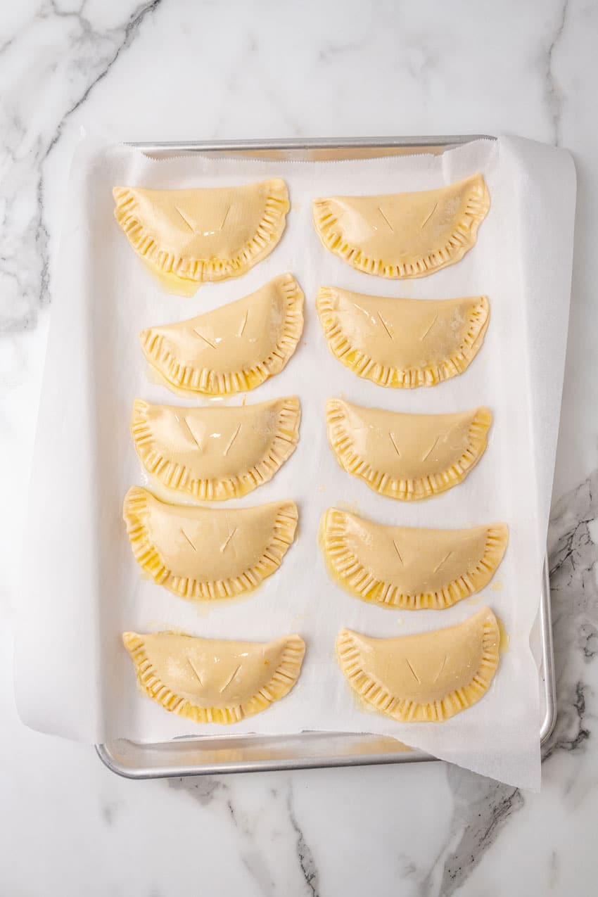 unbaked pumpkin hand pies arranged in two rows on a parchment paper lined baking sheet