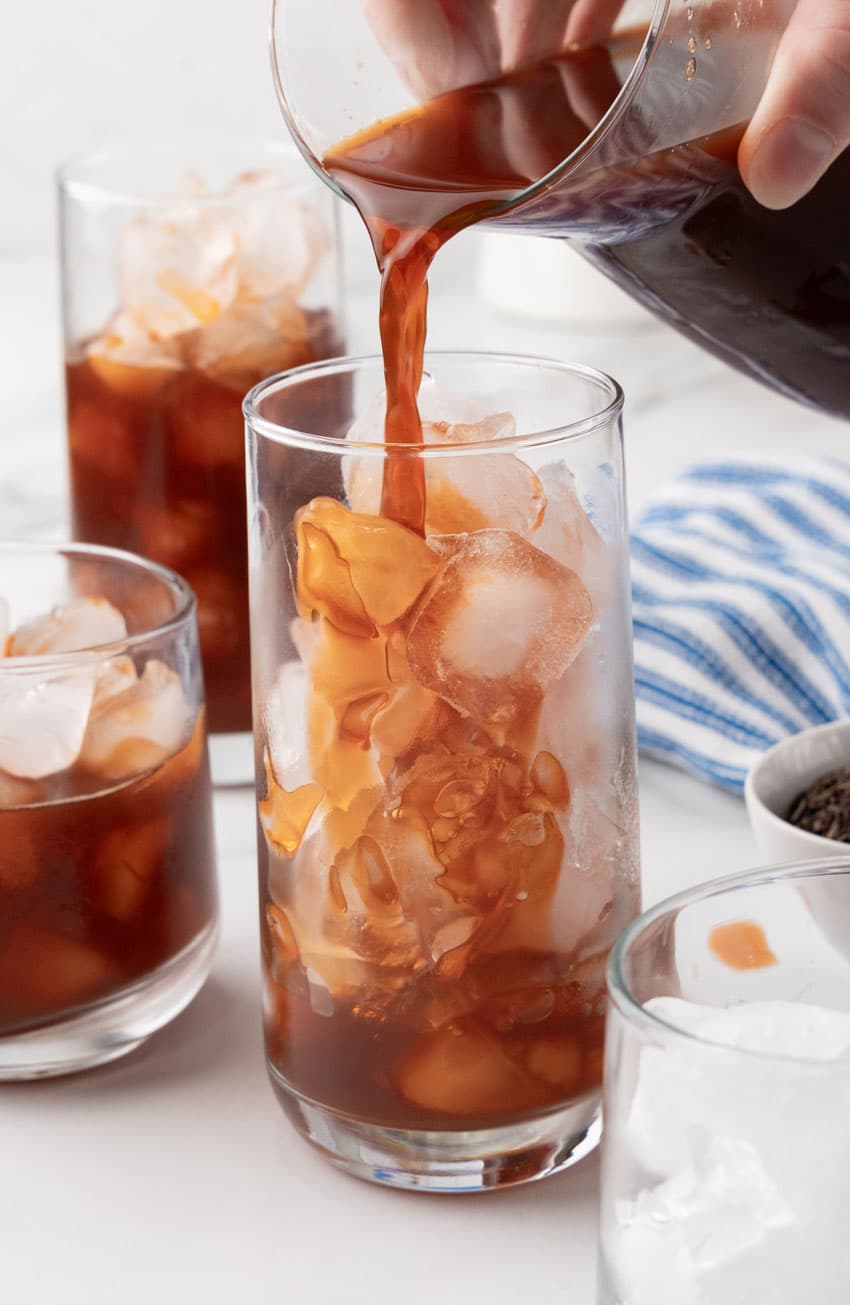 brewed black tea being poured over ice cubes into a tall drinking glass