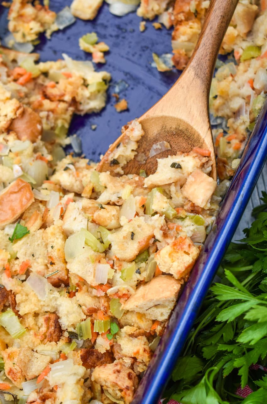 a wooden spoon scooping cheddar bay biscuit stuffing out of a blue casserole dish