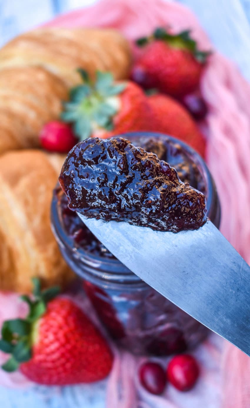 a wooden handled spreader holding up a scoop of homemade christmas jam