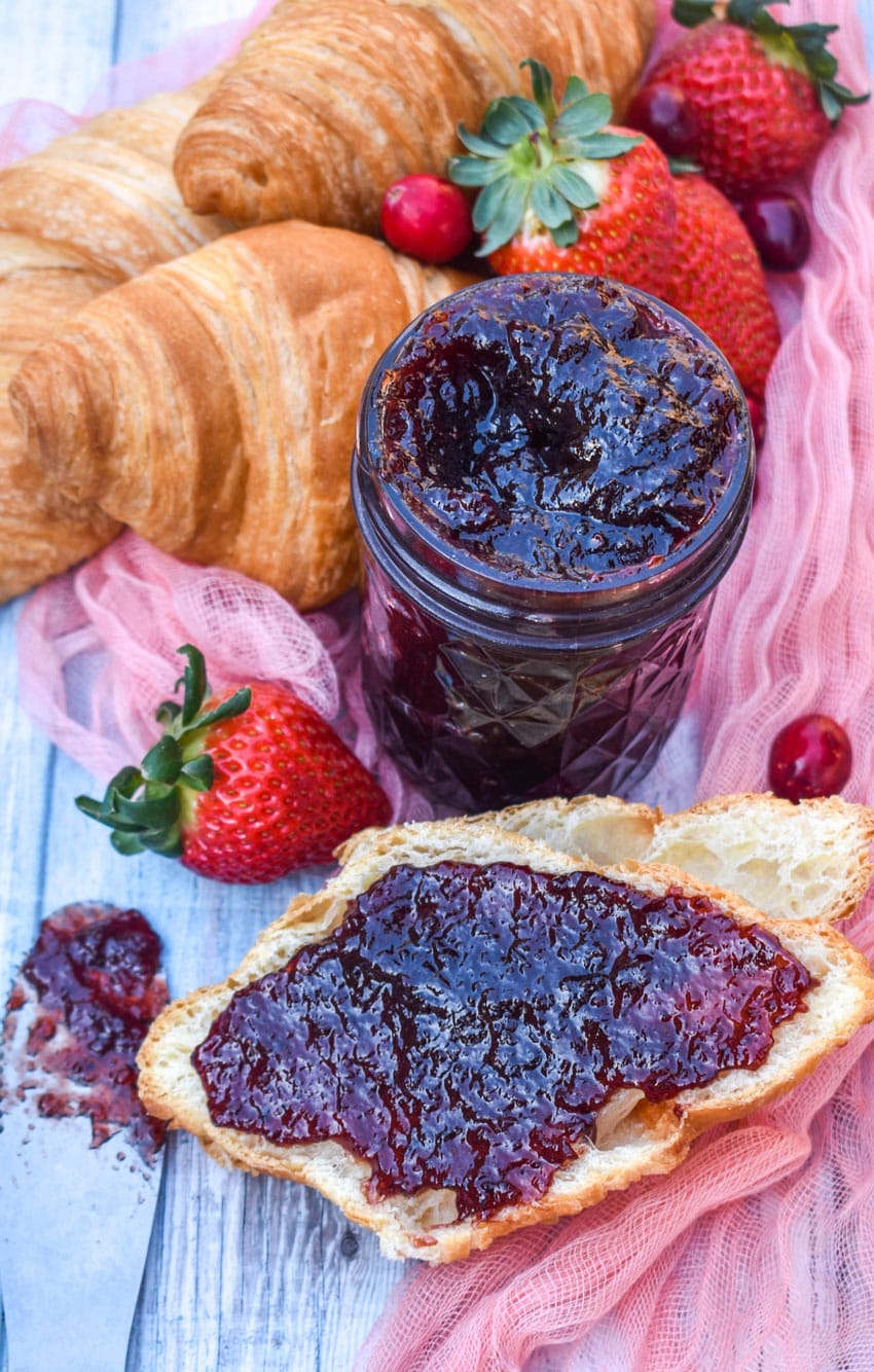 homemade christmas jam spread over half a croissant roll surrounded by fresh strawberries and cranberries