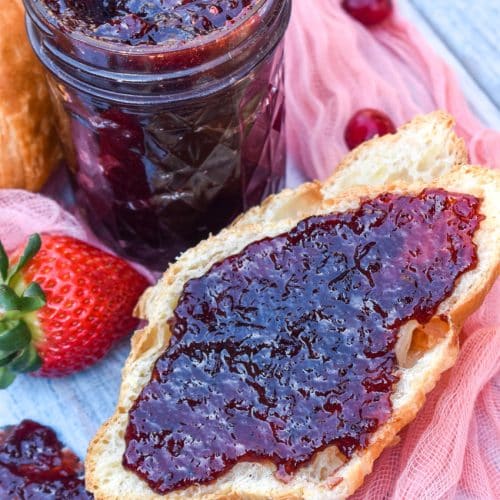 homemade christmas jam spread over half a croissant roll surrounded by fresh strawberries and cranberries