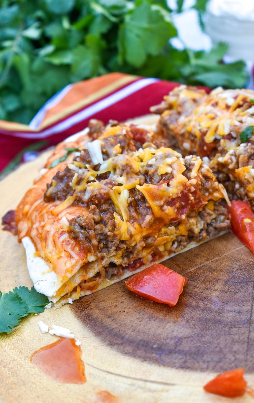 a quarter of a meaty double decker mexican pizza on a wooden cutting board