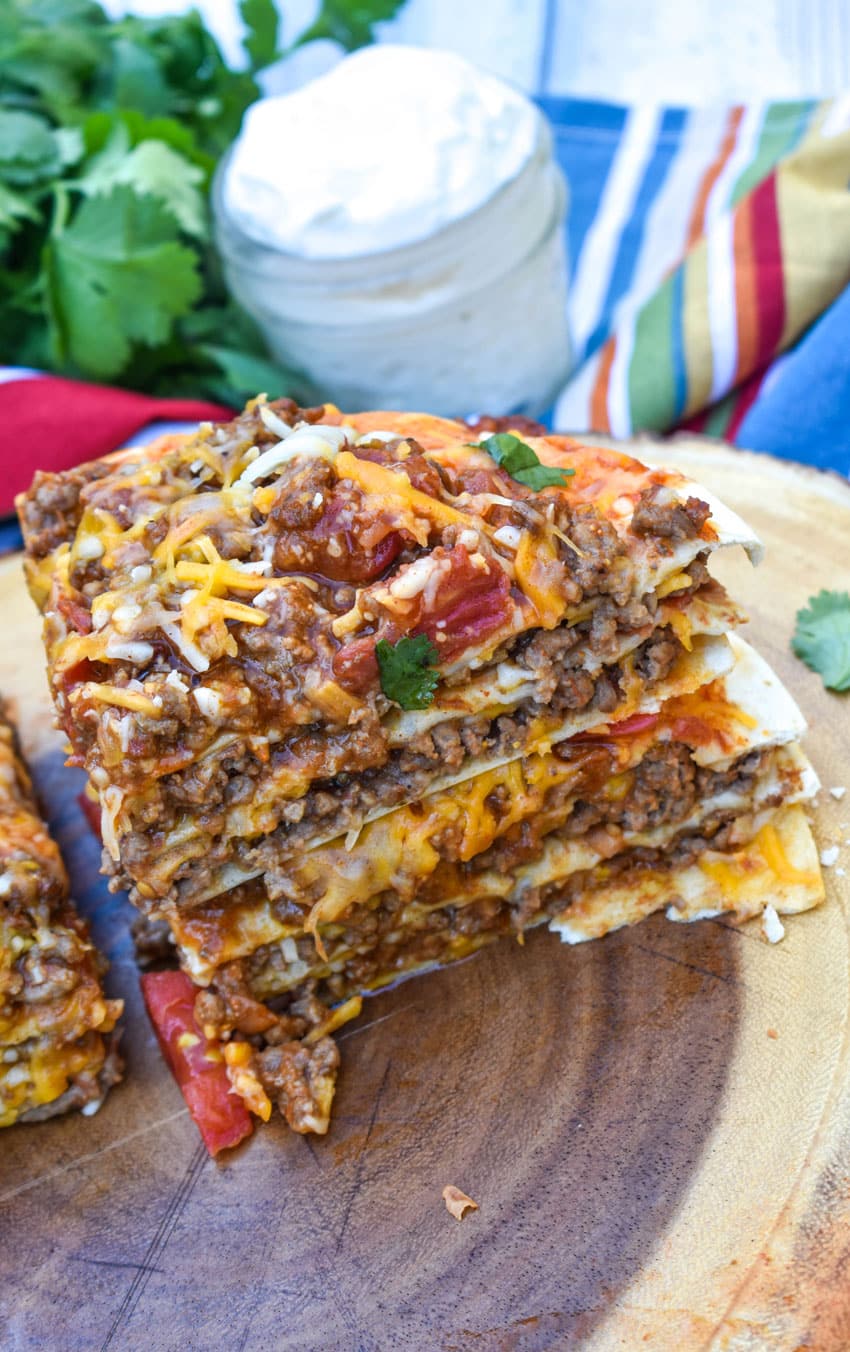 two quarters of a double decker mexican pizza stacked on top of each other on a wooden cutting board