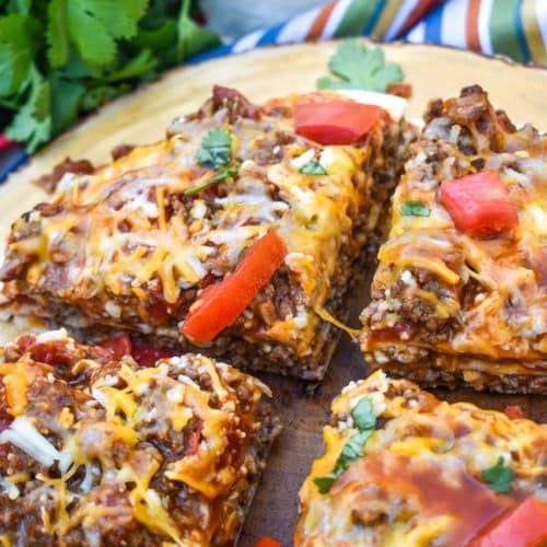 a meaty double decker mexican pizza sliced into four quarters on a wooden cutting board