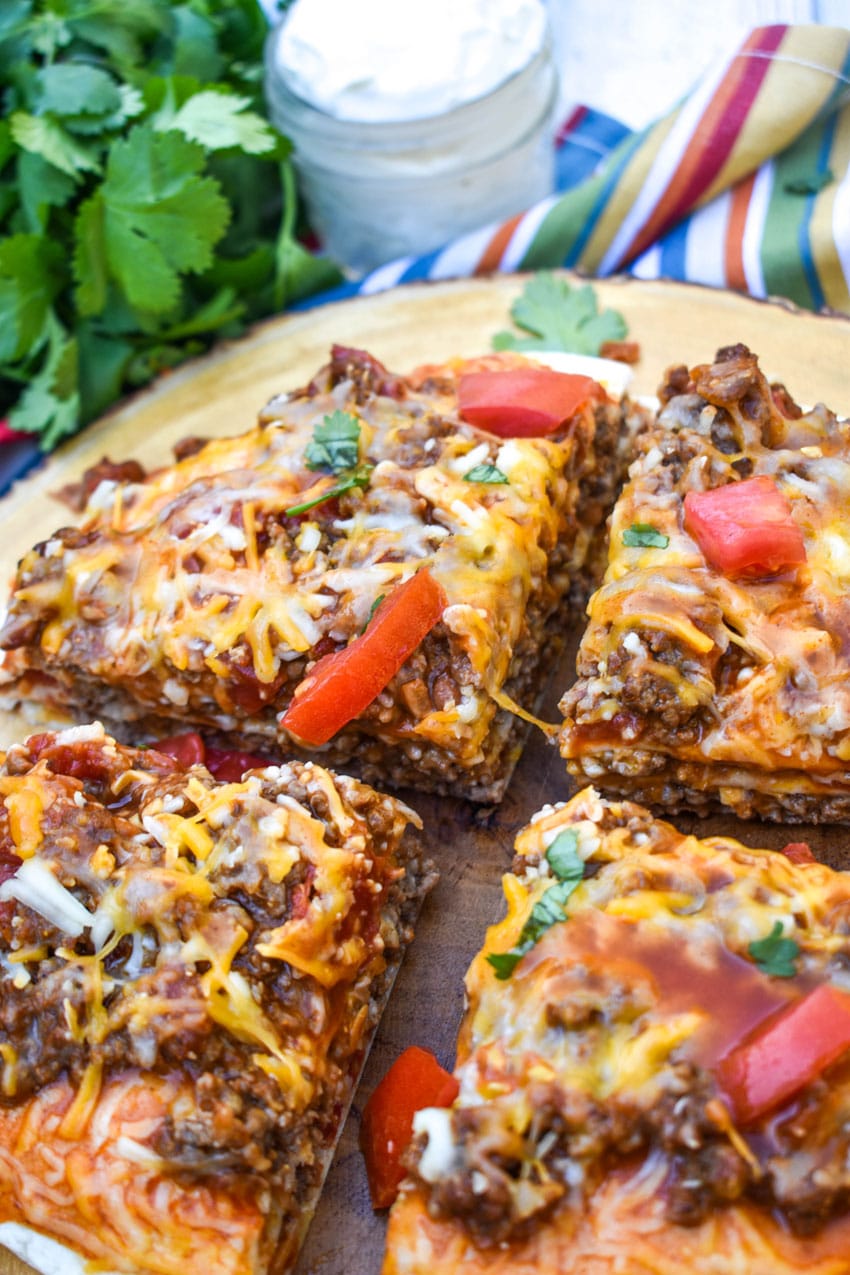 a meaty double decker mexican pizza sliced into four quarters on a wooden cutting board