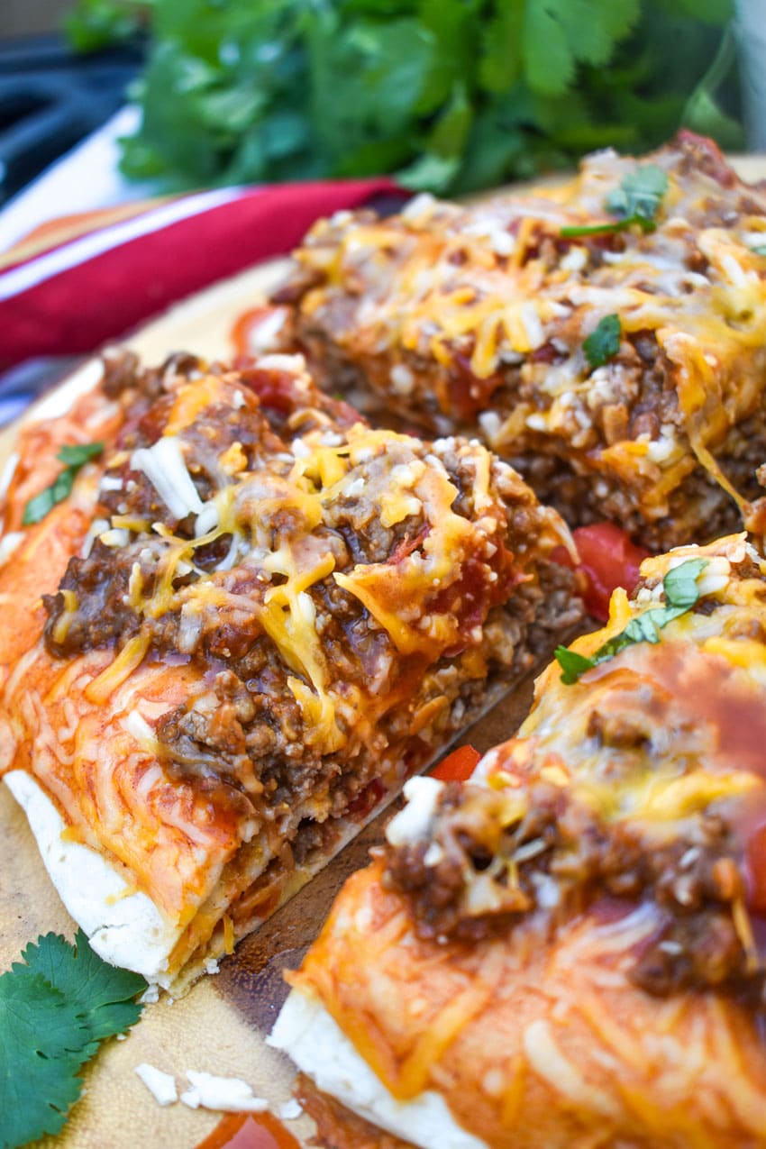 a meaty double decker mexican pizza sliced into four quarters on a wooden cutting board