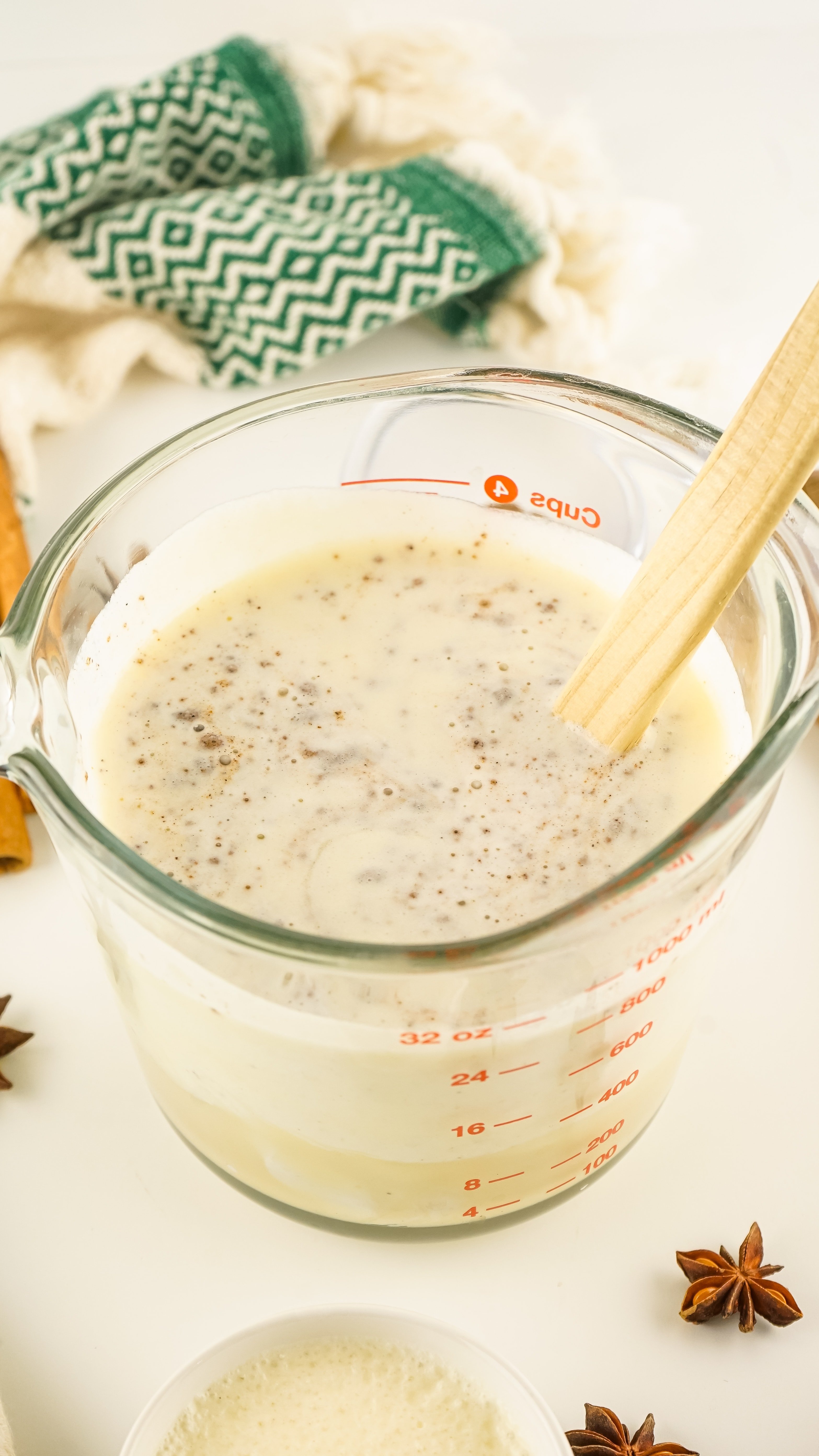 a wooden spoon stirring together the ingredients for eggnog coffee creamer in a glass measuring bowl