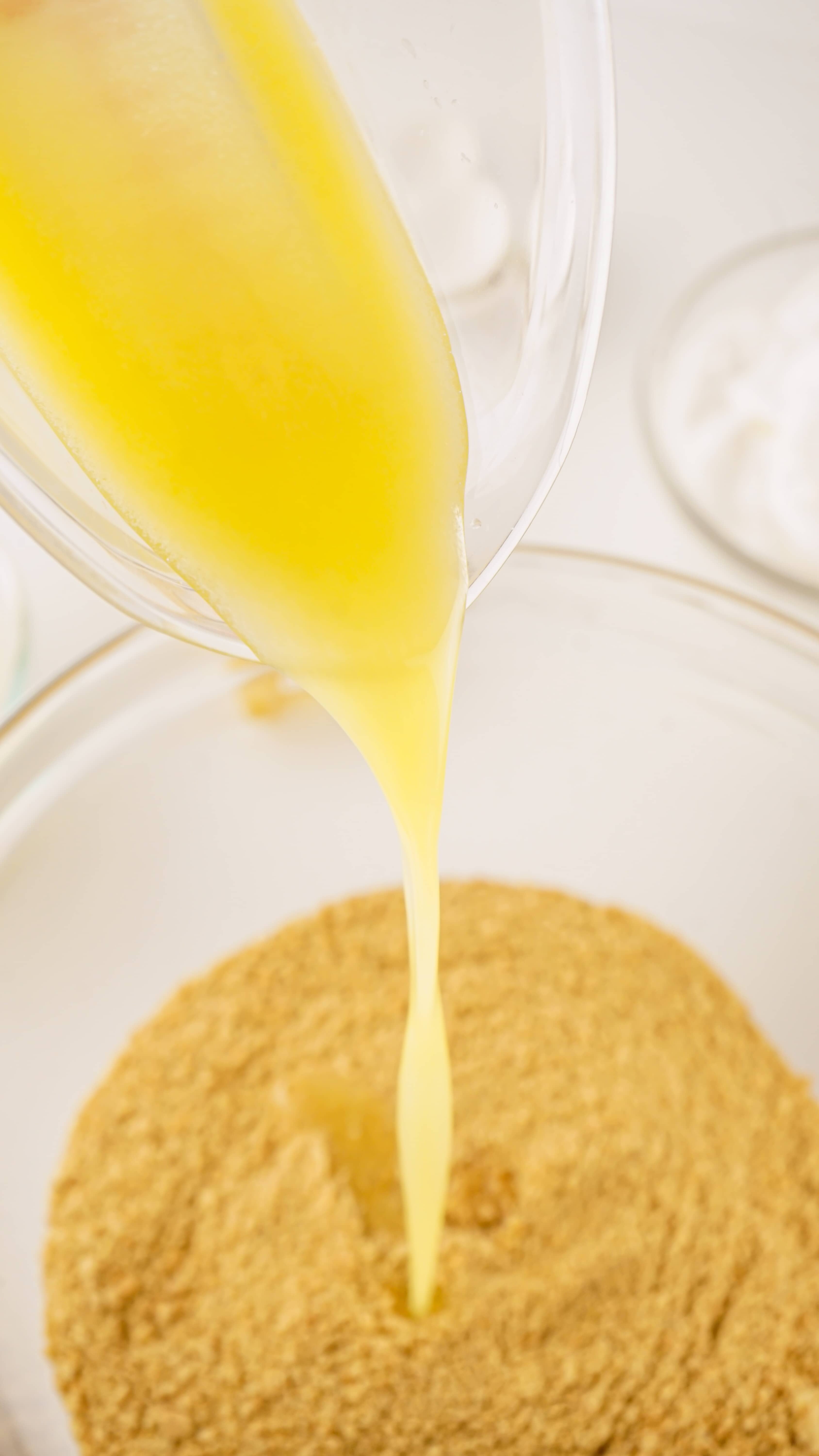 melted butter being poured into a mixing bowl with crushed graham cracker crumbs