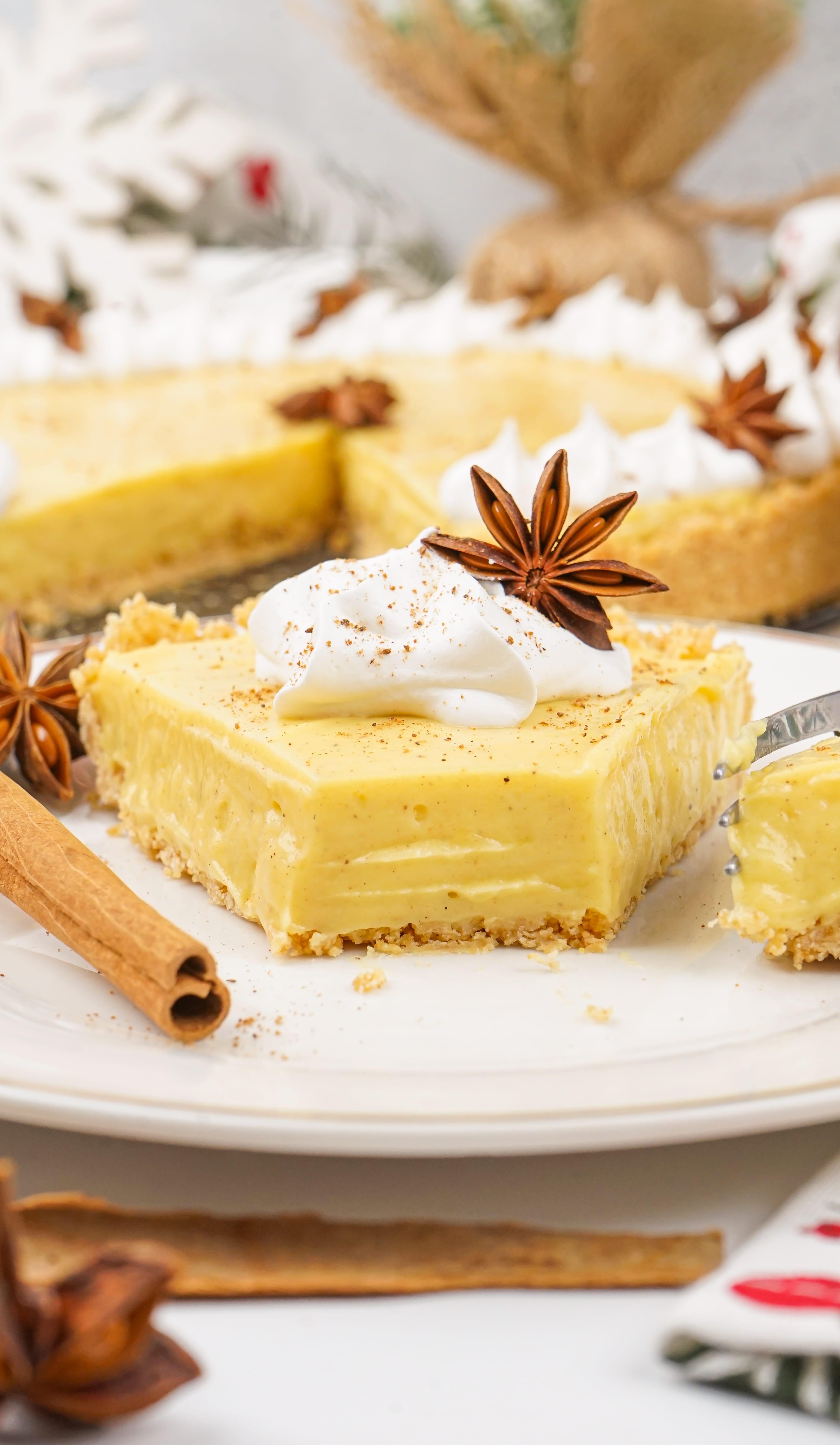 a slice of no bake eggnog pie on a white plate with cinnamon sticks and a silver fork on the side