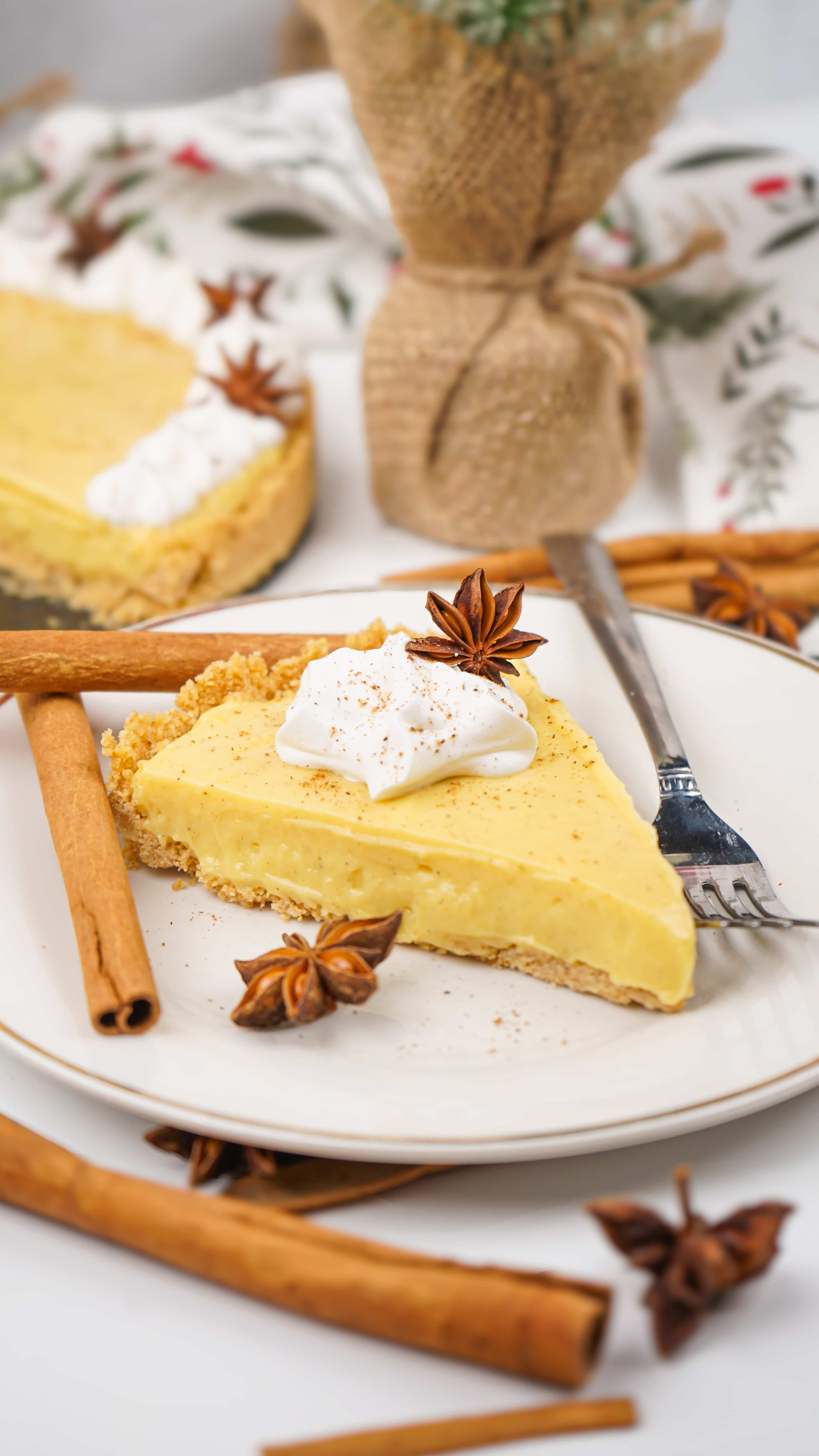 a slice of no bake eggnog pie on a white plate with cinnamon sticks and a silver fork on the side