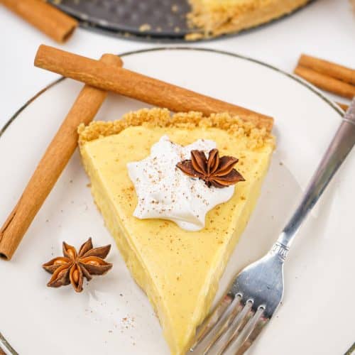 a slice of no bake eggnog pie on a white plate with cinnamon sticks and a silver fork on the side