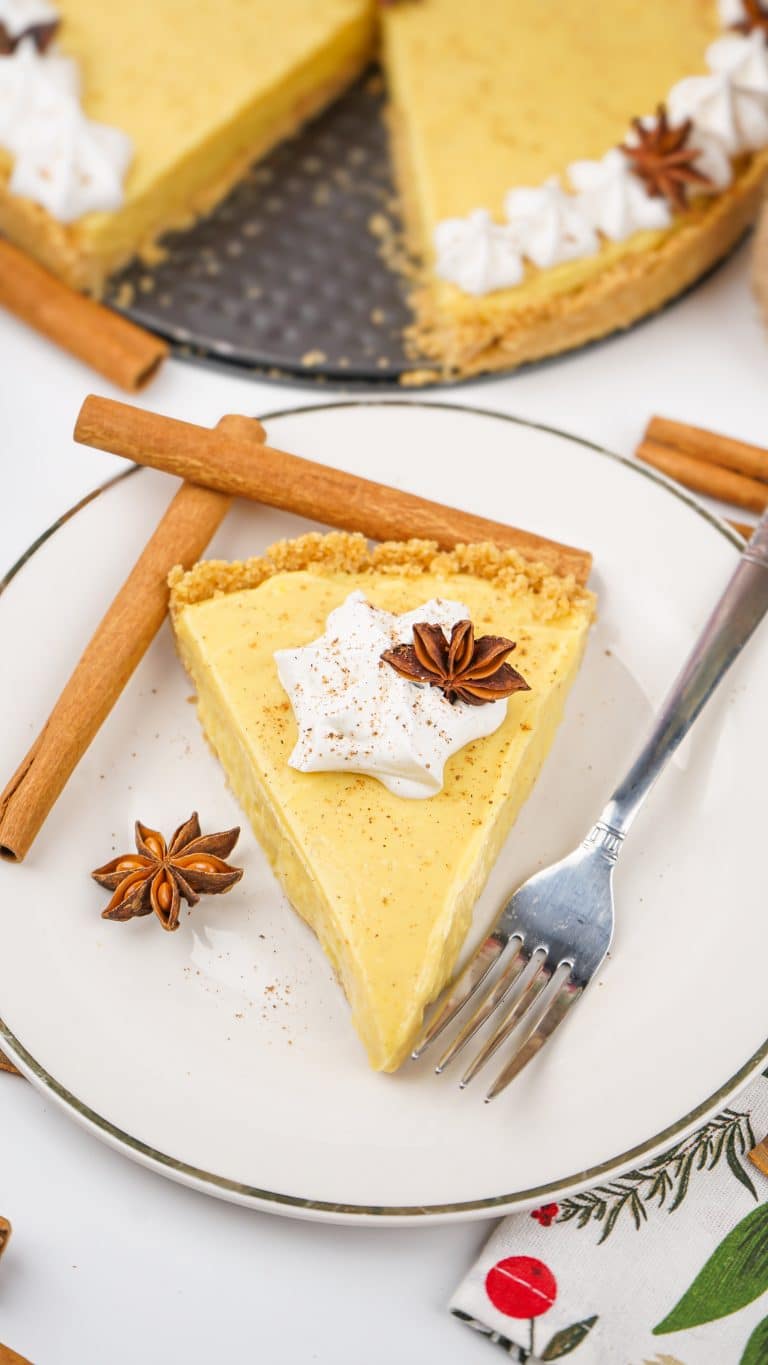 a slice of no bake eggnog pie on a white plate with cinnamon sticks and a silver fork on the side