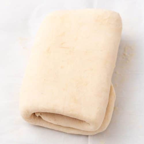 a tri folded sheet of homemade puff pastry resting on a piece of white parchment paper