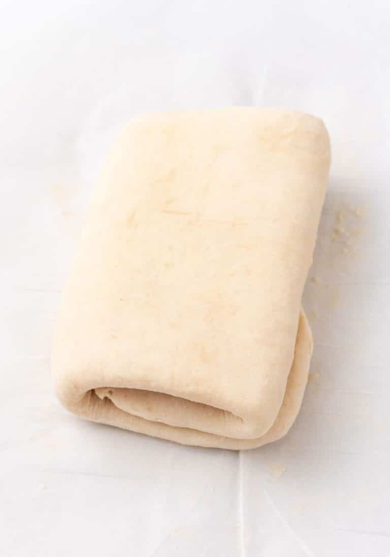 a tri folded sheet of homemade puff pastry resting on a piece of white parchment paper