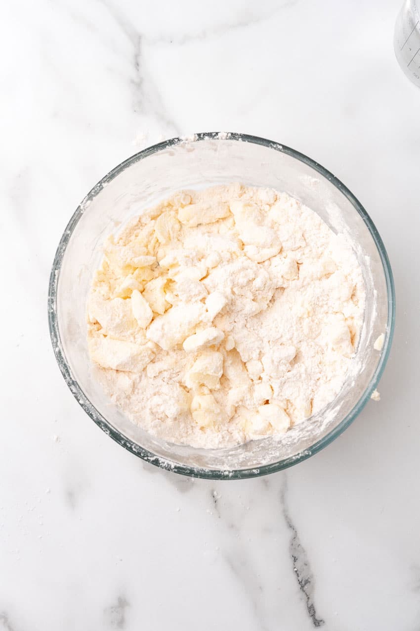 pieces of cold butter being cut into flour in a glass mixing bowl