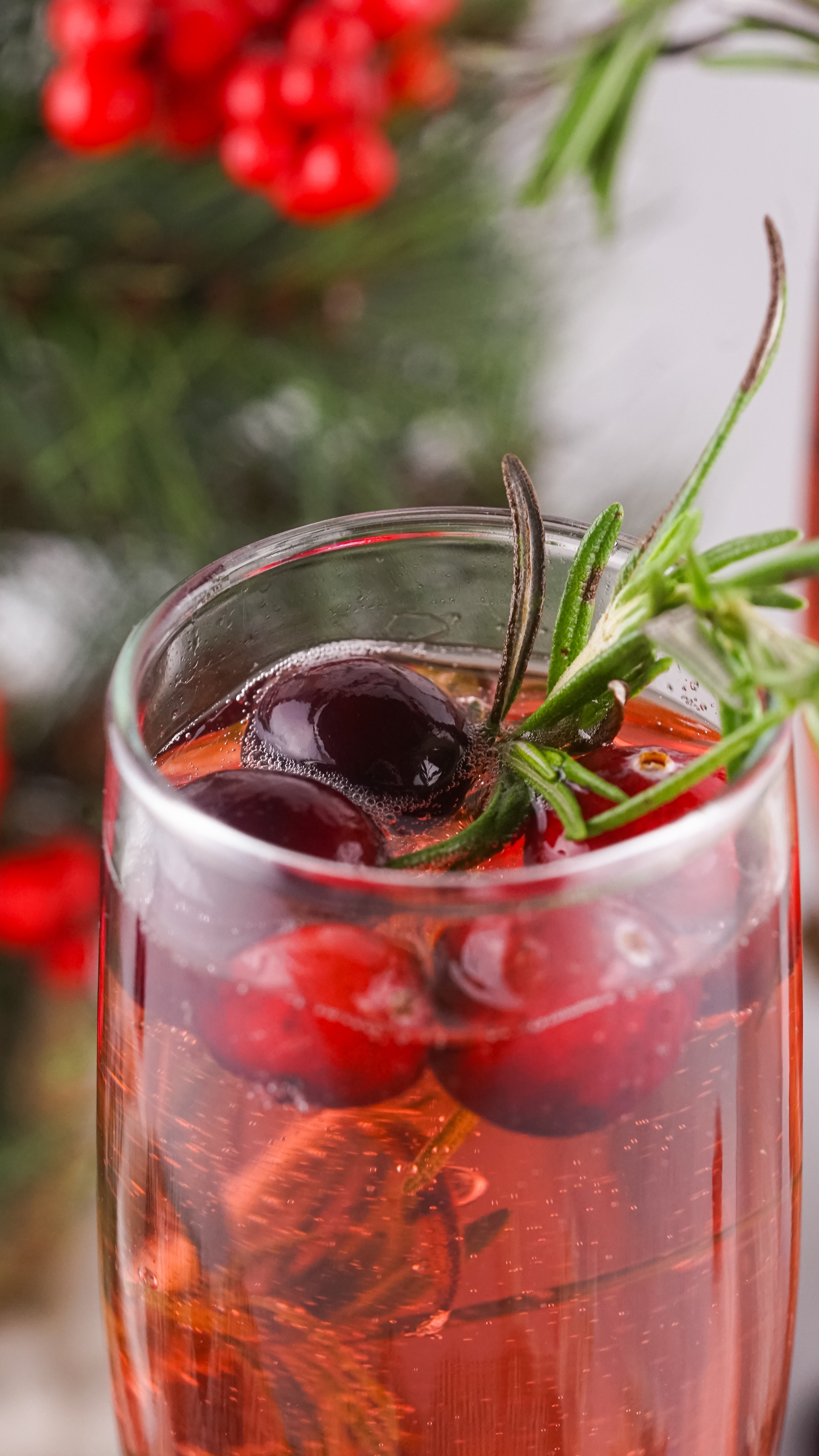 a closeup of a cranberry mimosa in  a glass garnished with fresh cranberries and sprigs of rosemary