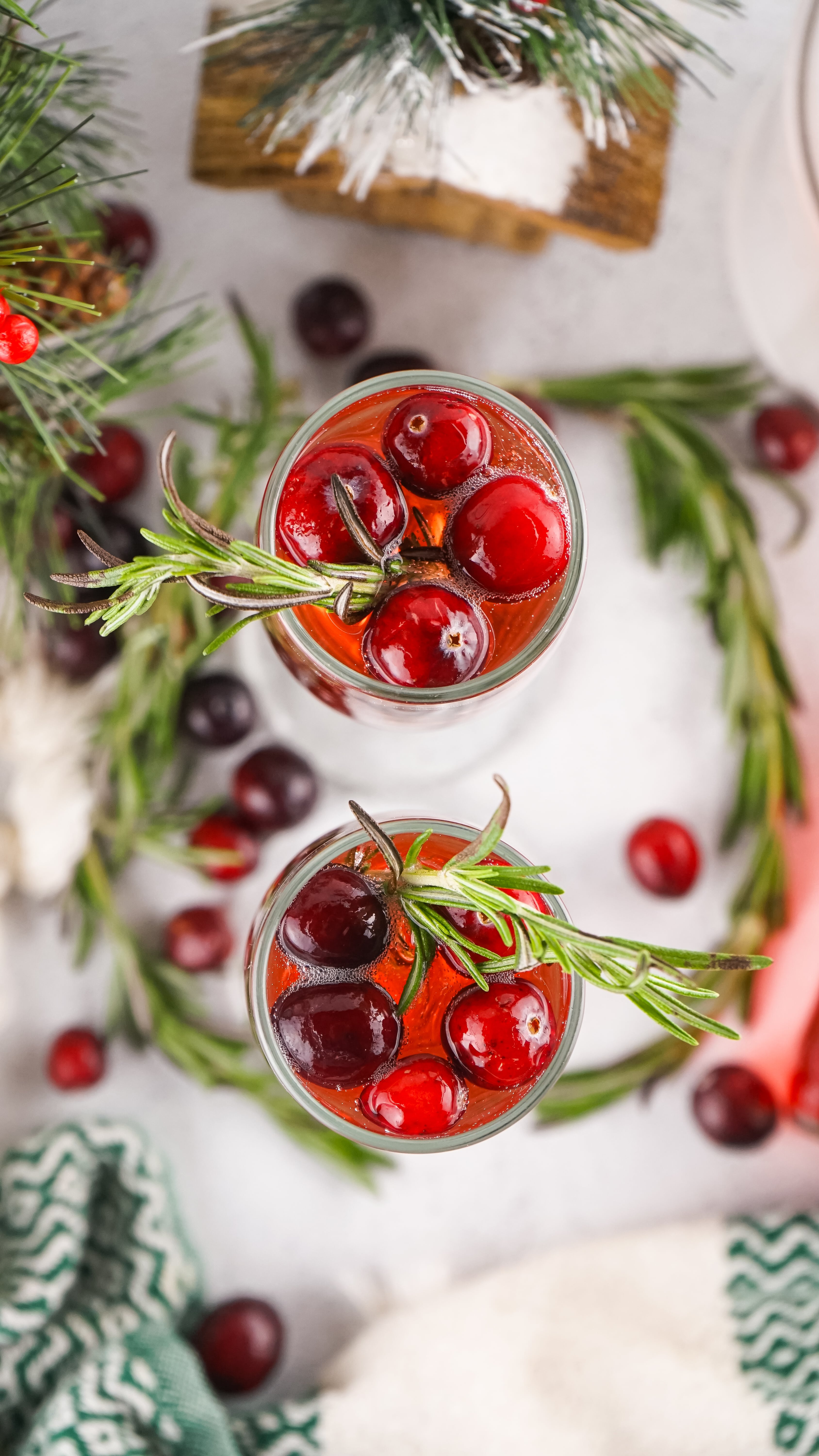 an overhead image showing two glasses filled with cranberry mimosas and garnished with sprigs of fresh rosemary and fresh cranberries