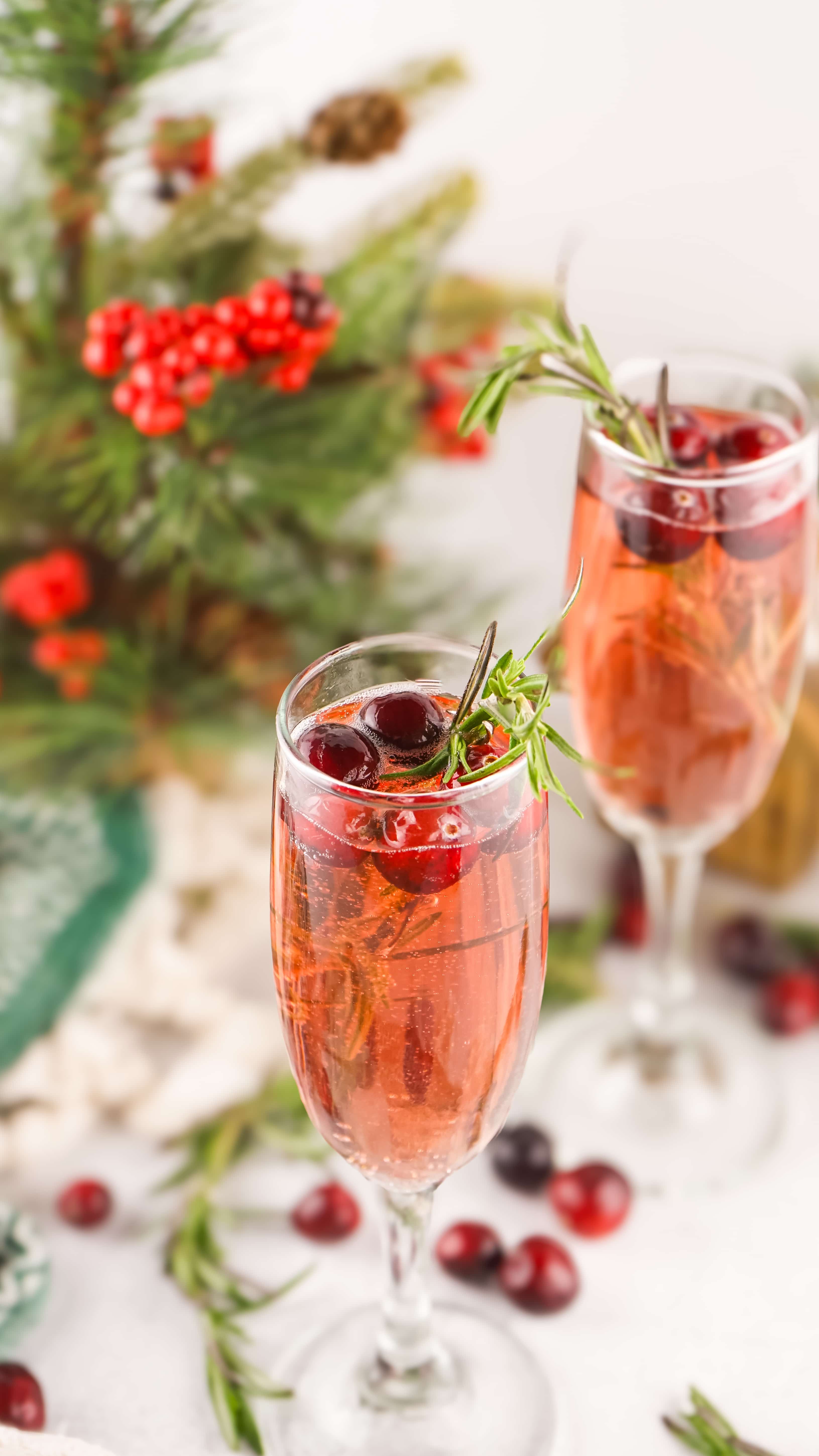 cranberry mimosas in a fluted glass with sprigs of fresh rosemary and fresh cranberries in the background