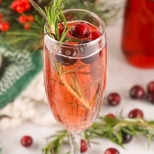 cranberry mimosas in a fluted glass with sprigs of fresh rosemary and fresh cranberries in the background