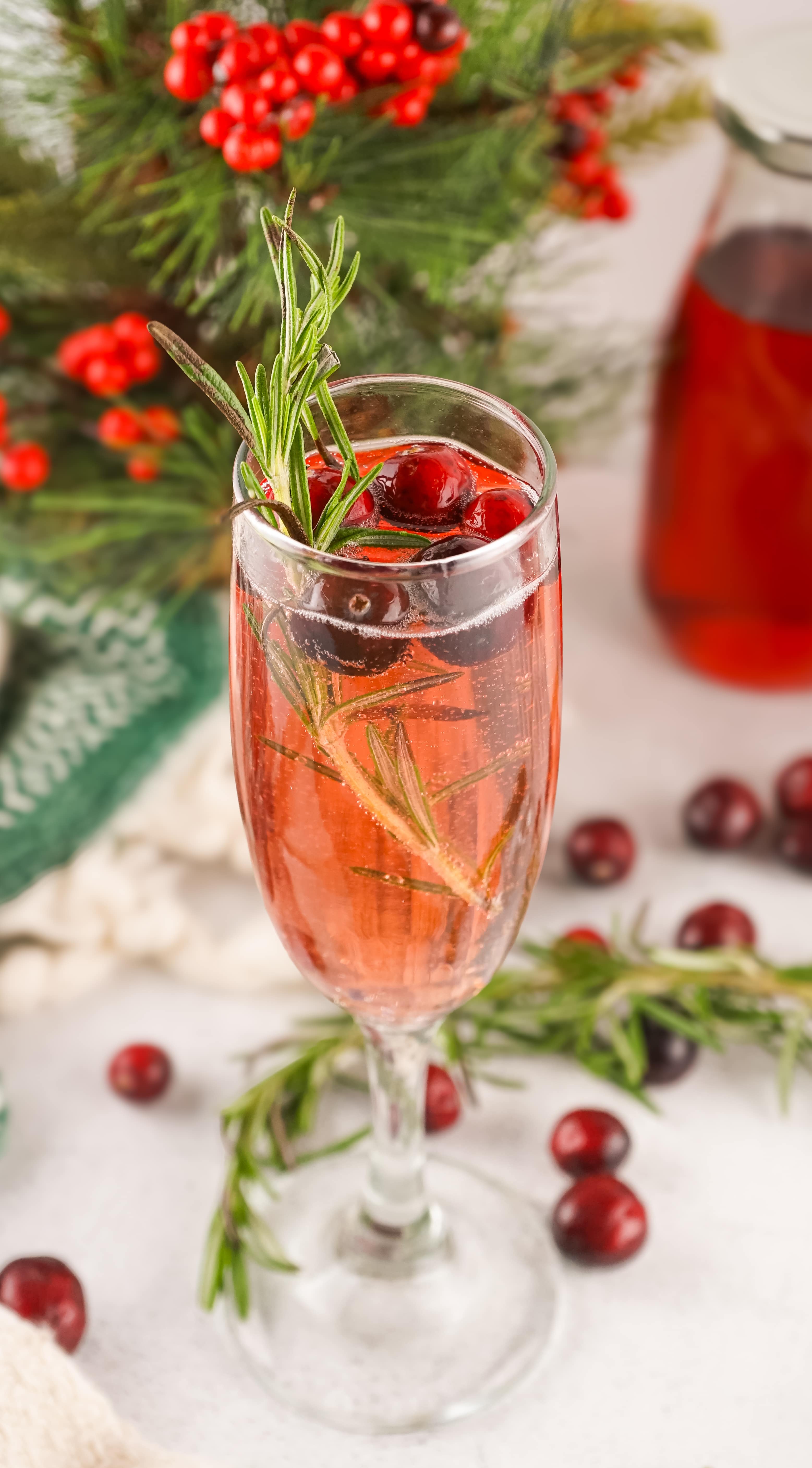 cranberry mimosas in a fluted glass with sprigs of fresh rosemary and fresh cranberries in the background