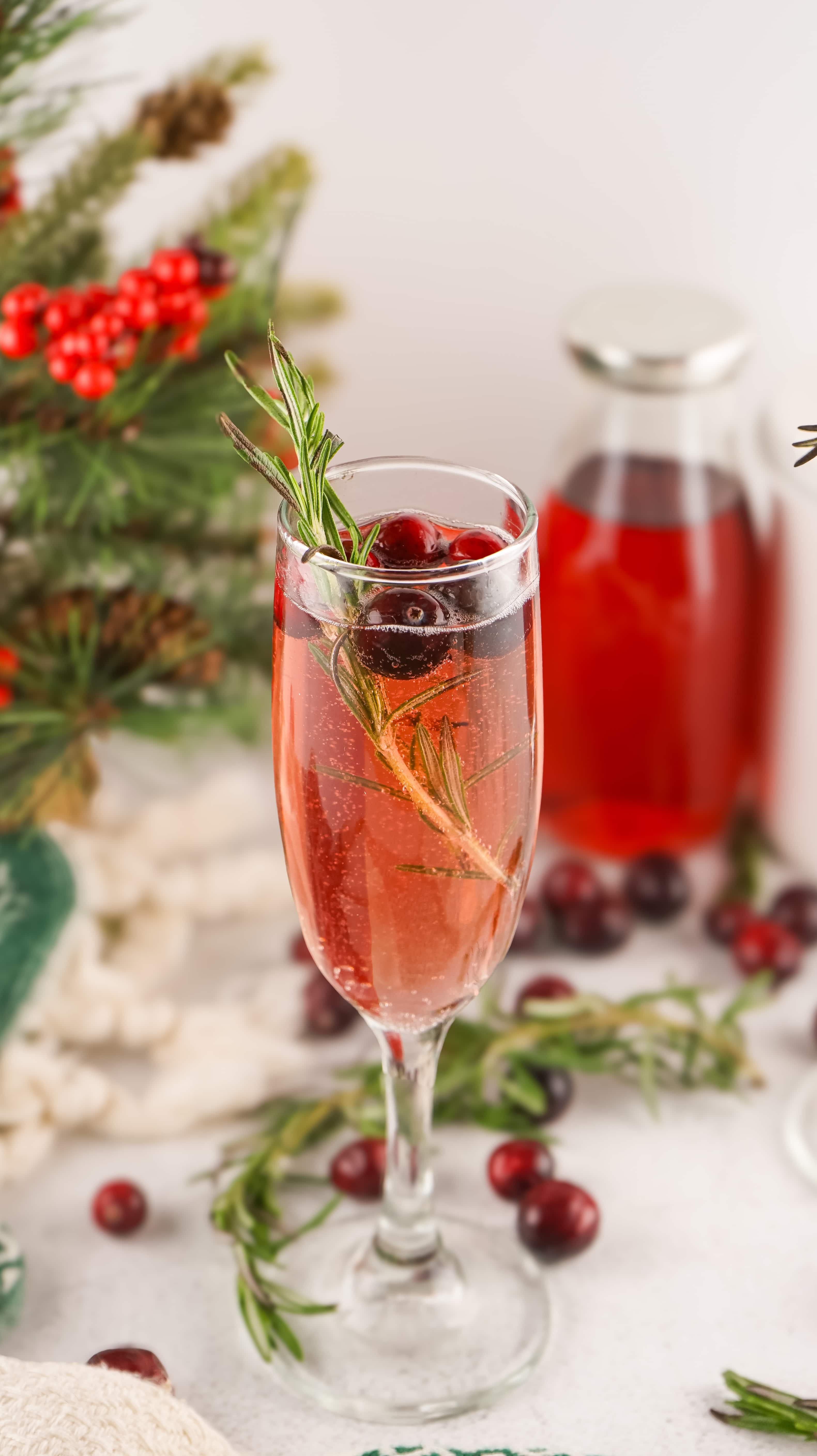 cranberry mimosas in a fluted glass with sprigs of fresh rosemary and fresh cranberries in the background