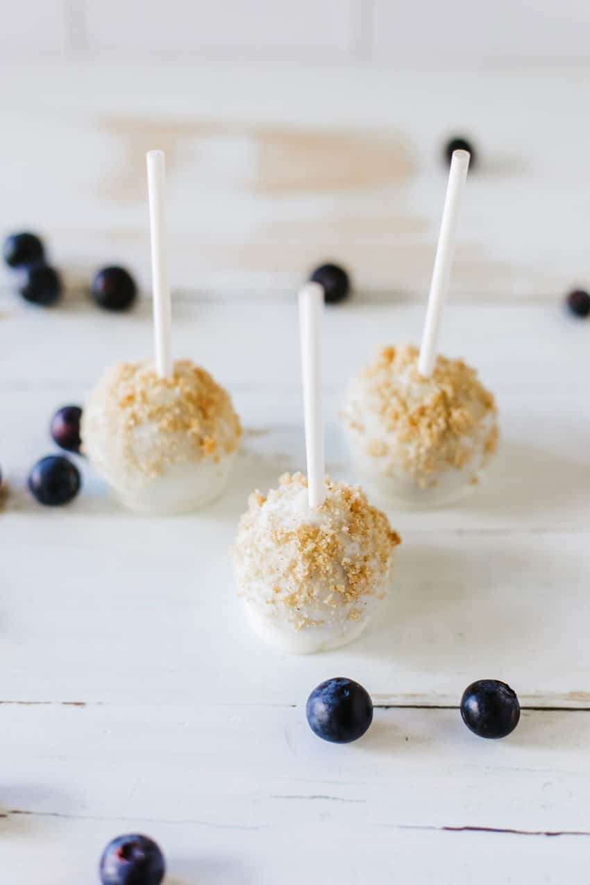 streusel coated blueberry muffin cake pops sitting on a wooden table with fresh blueberries