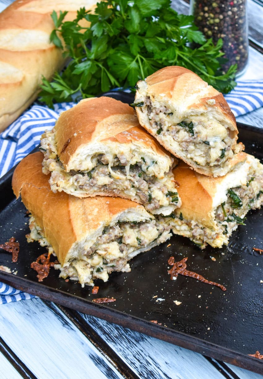 slices of sausage stuffed french bread sandwich stacked together on a metal baking sheet pan