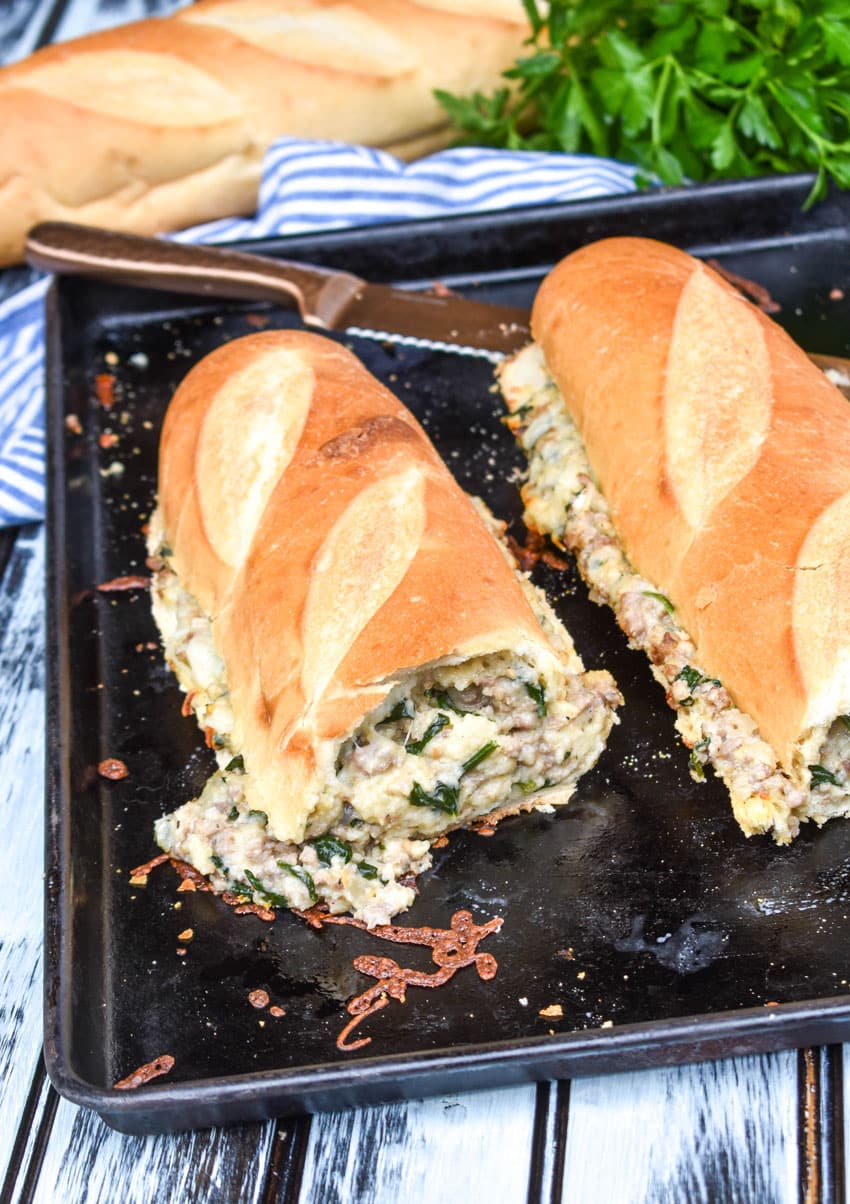 two pieces of sausage stuffed french bread sandwich stacked together on a metal baking sheet pan