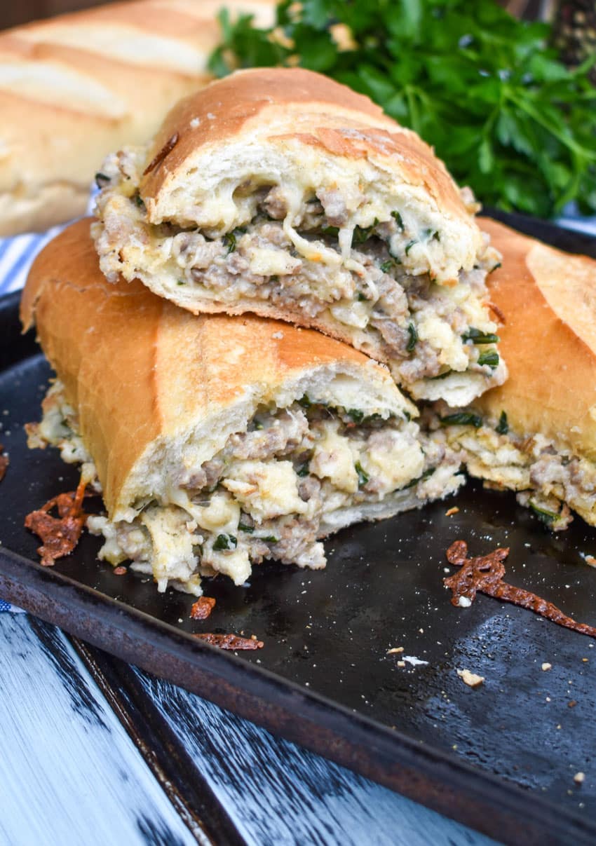 two halves of a sausage stuffed french bread sandwich stacked together on a metal baking sheet pan