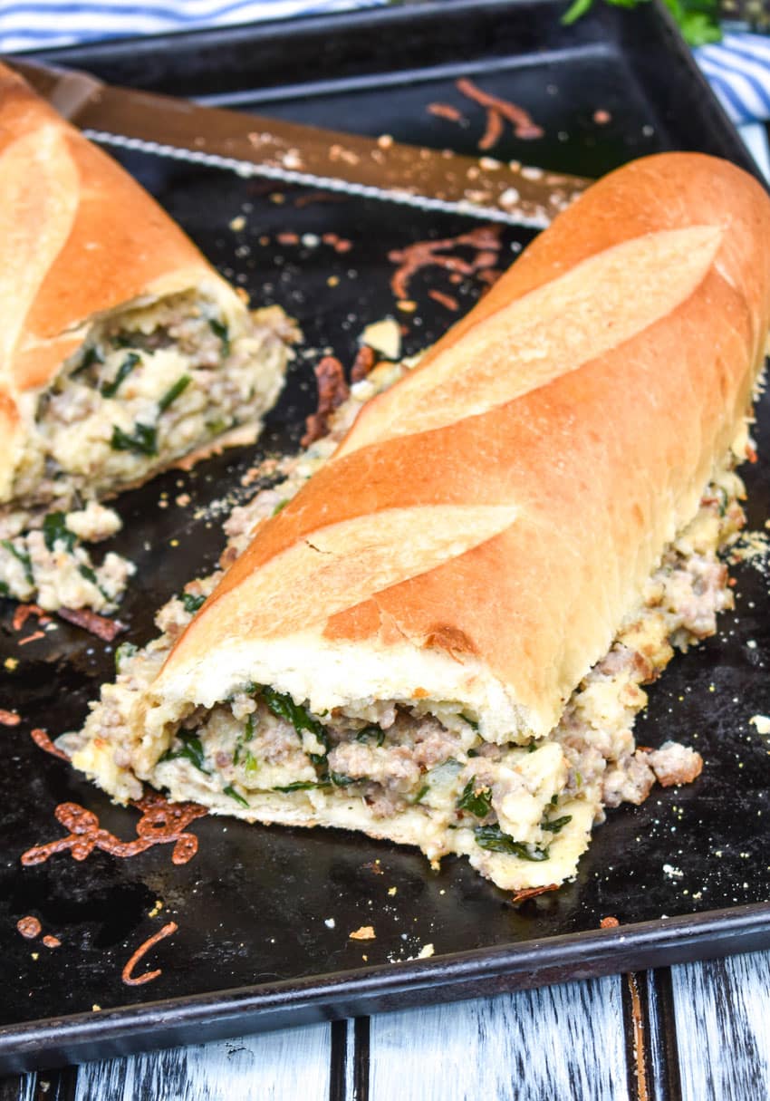 two pieces of sausage stuffed french bread sandwich stacked together on a metal baking sheet pan