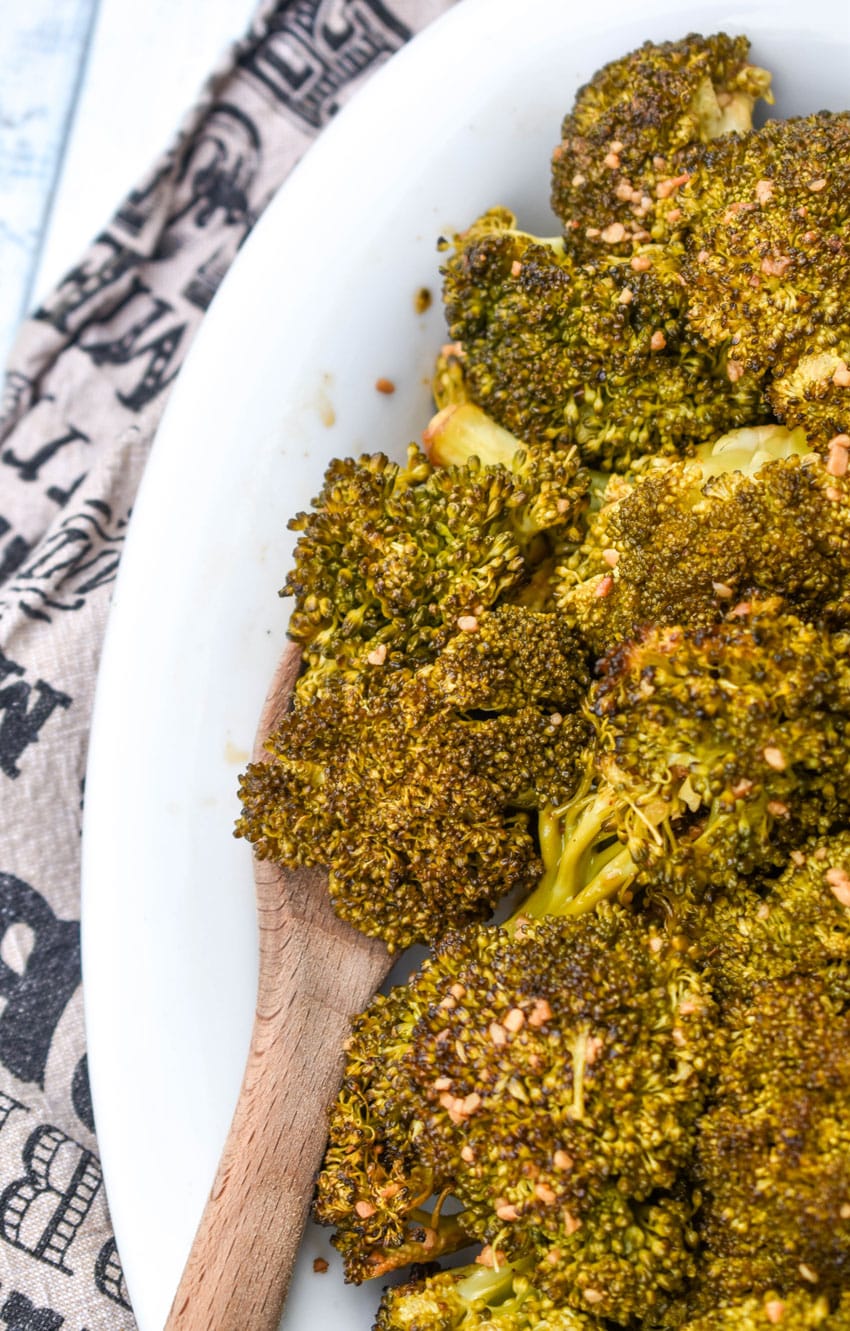 a wooden spoon scooping smoked broccoli out of a white serving dish