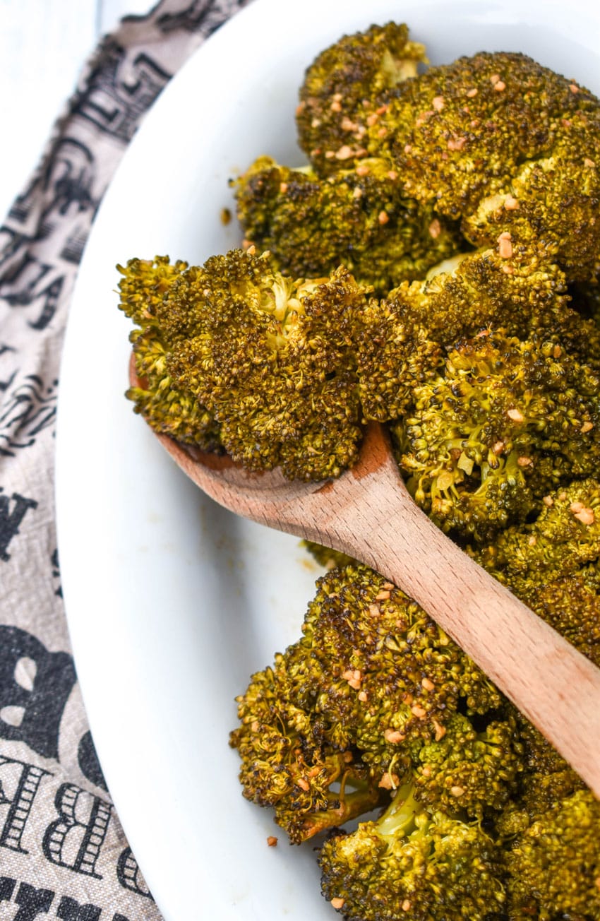 a wooden spoon scooping smoked broccoli out of a white serving dish