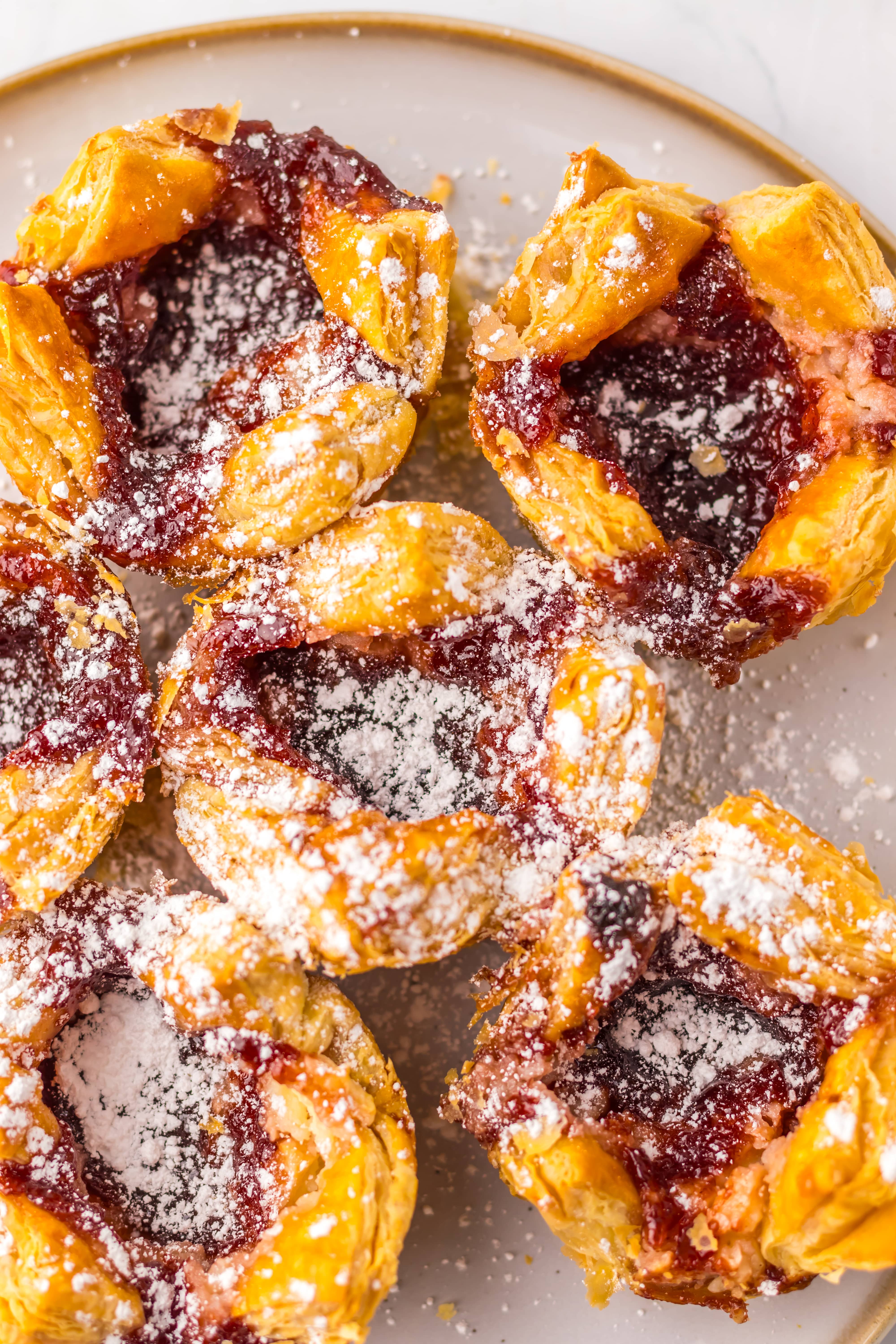 a close up of powdered sugar sprinkled sugar plum danishes on a wooden table