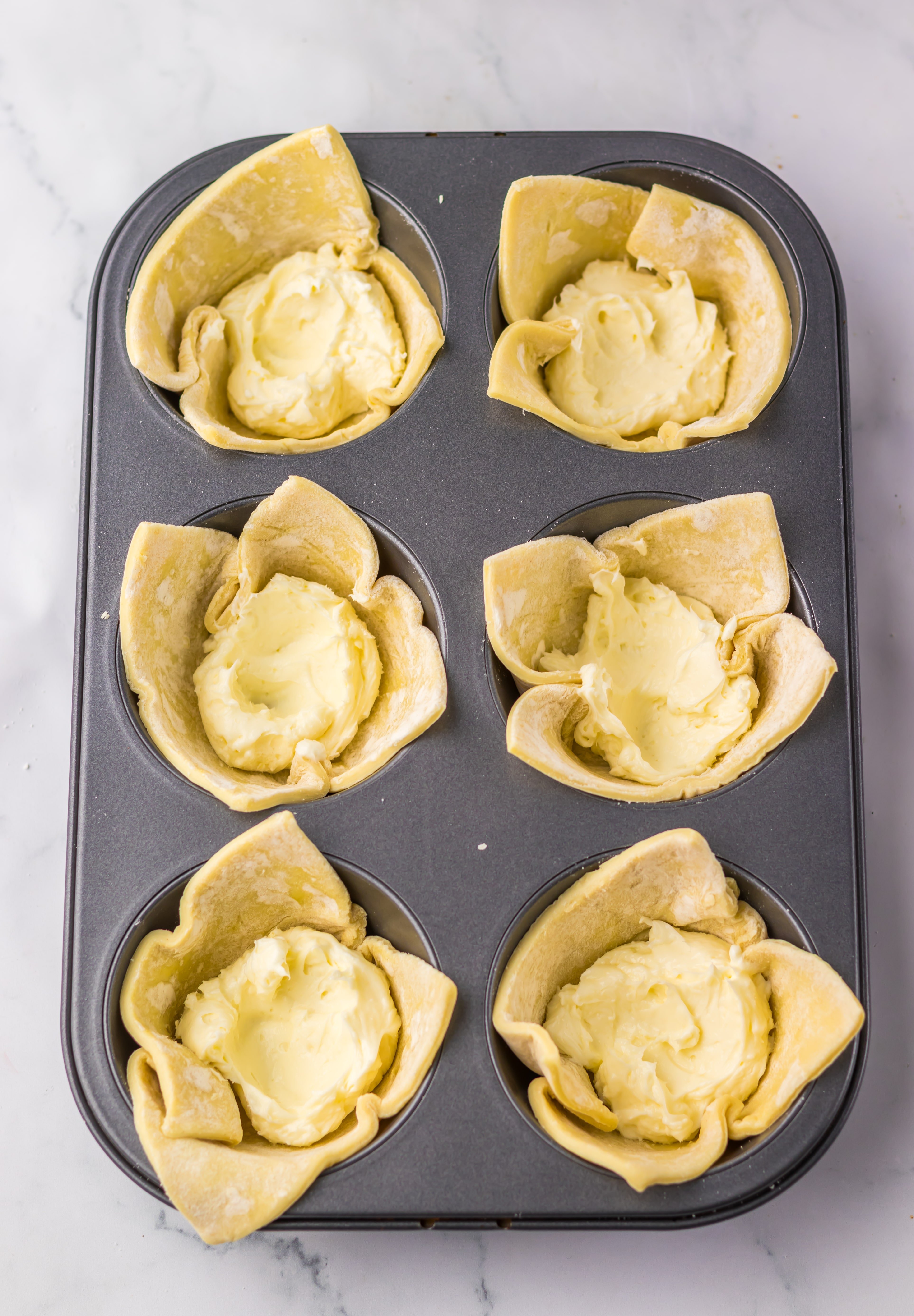 puff pastry squares filled with whipped cream cheese in a jumbo metal muffin pan