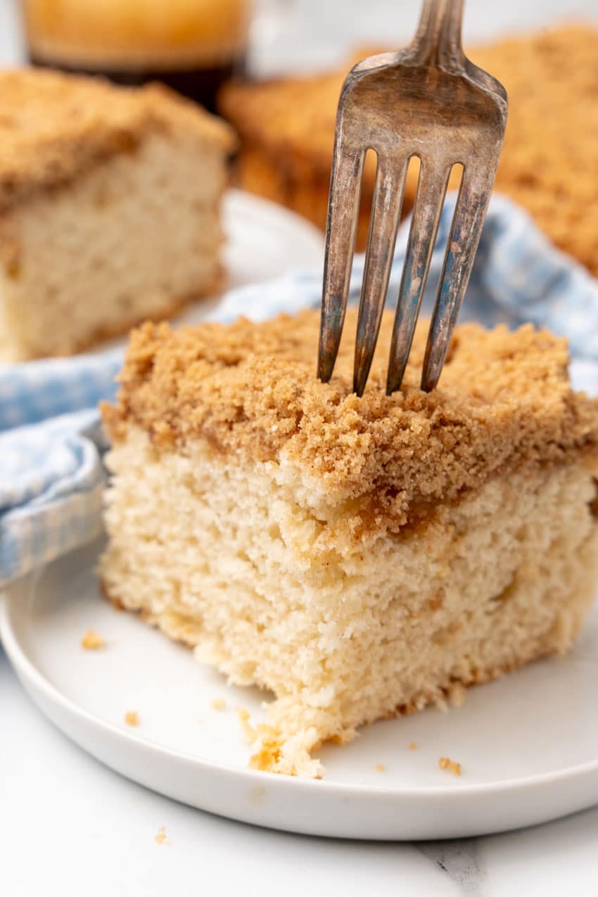 a silver fork digging into a corner of a slice of bisquick coffee cake on a small white dessert plate