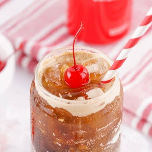 fluffy coke in a glass jar topped with a maraschino cherry