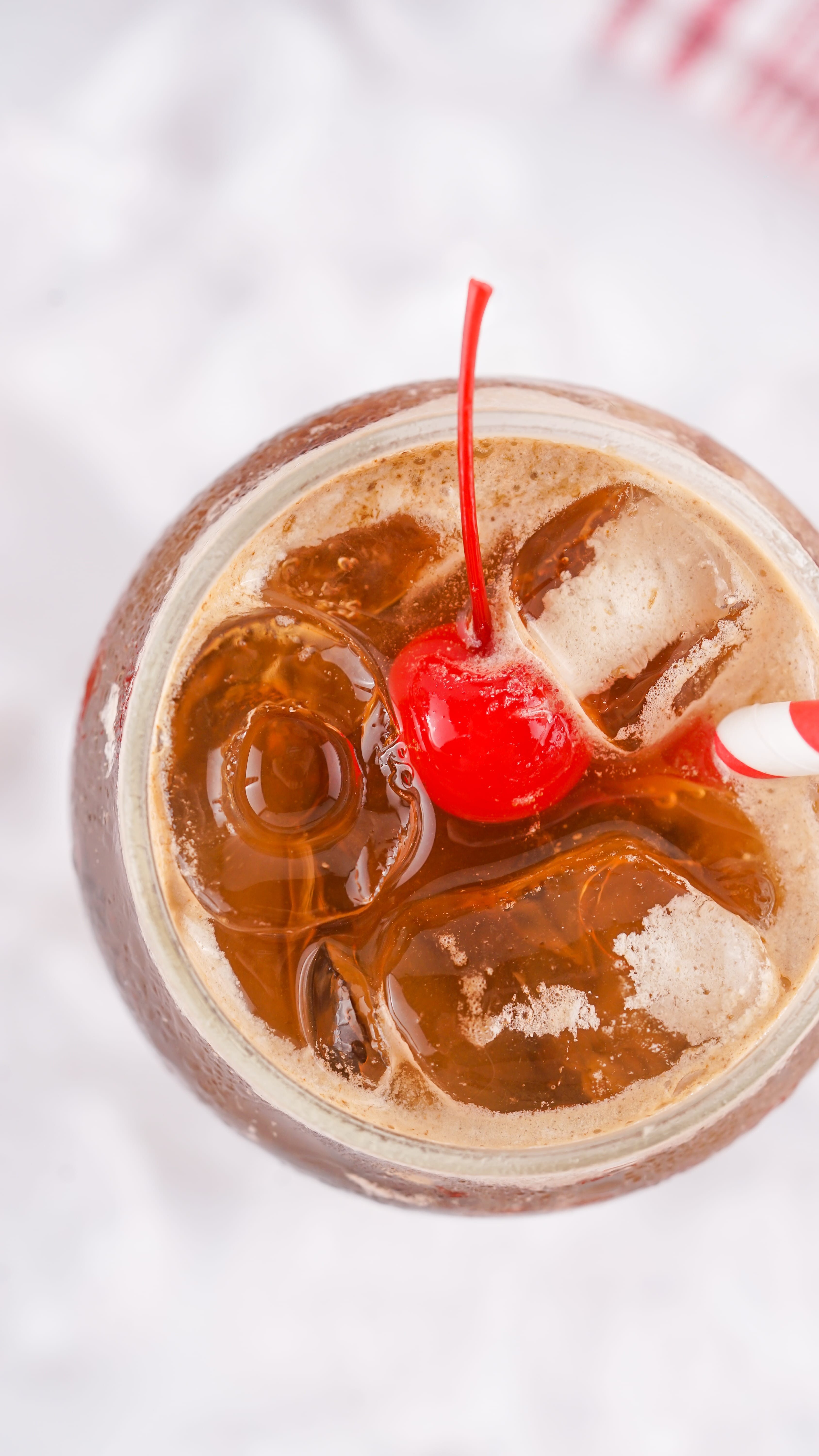 an overhead image showing a vintage fluffy coke in a glass jar topped with a maraschino cherry