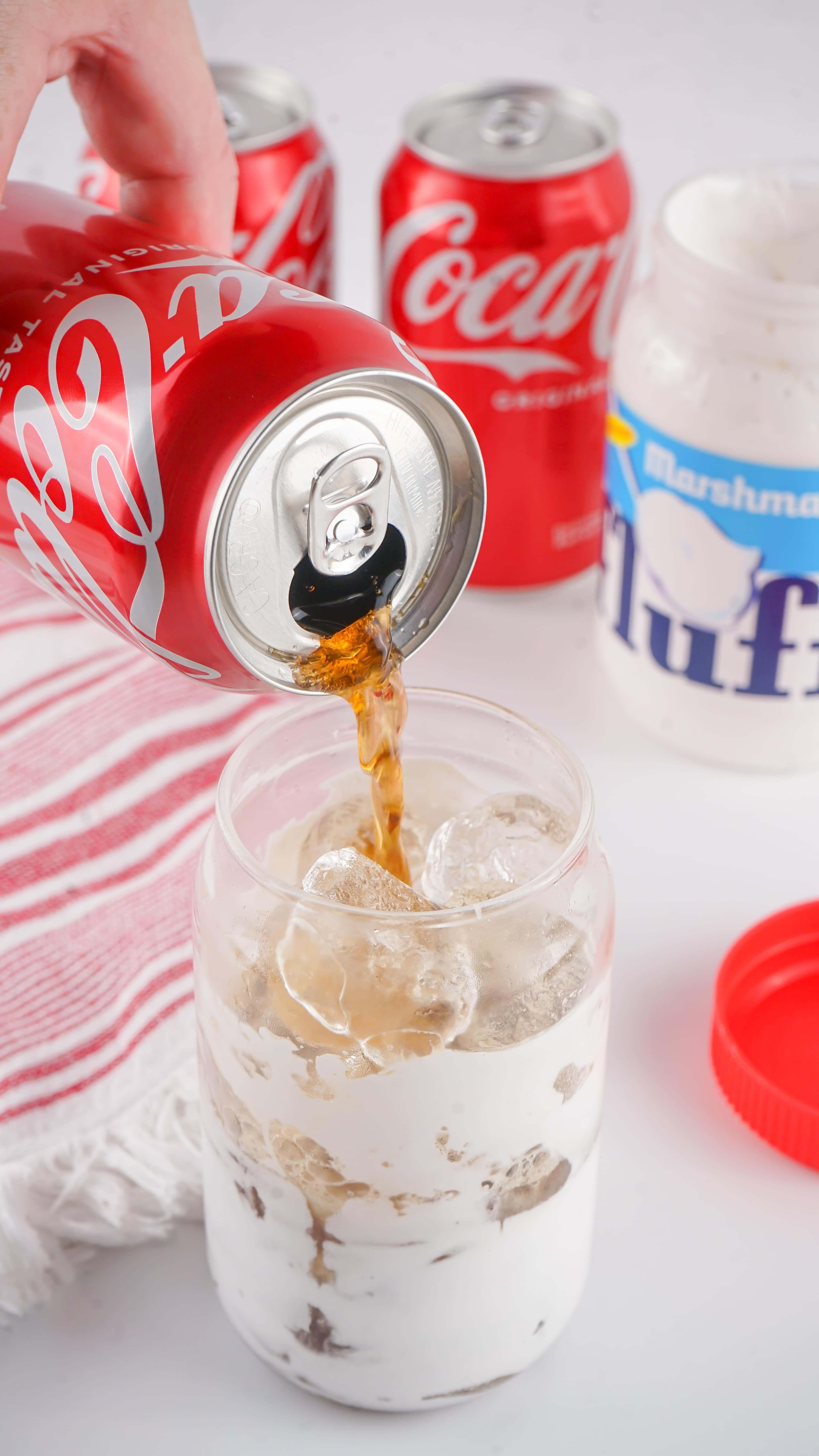 classic coca cola being poured over ice into a marshmallow fluff coated glass jar