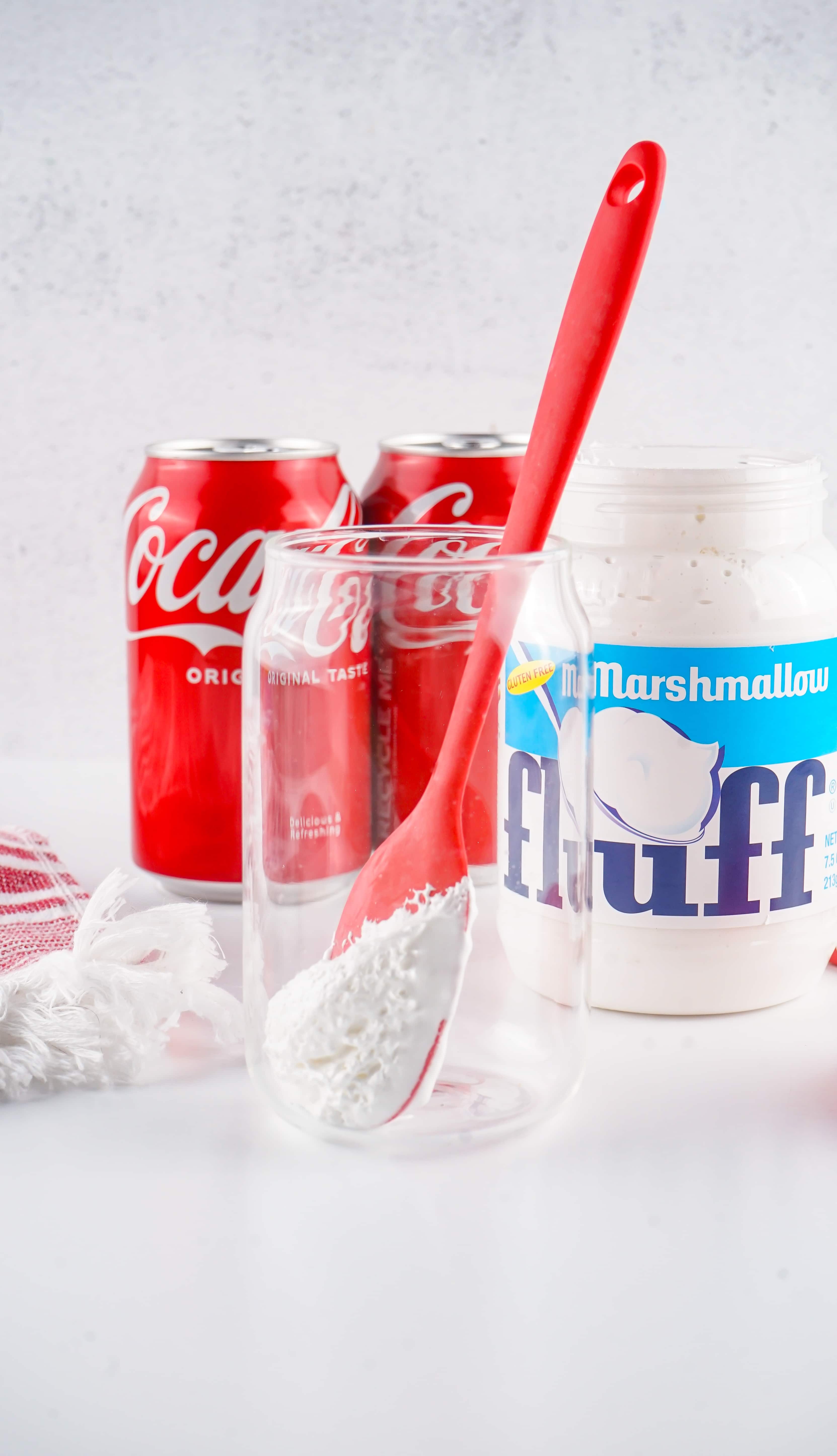 a red spatula spreading marshmallow fluff on the inside of a glass jar